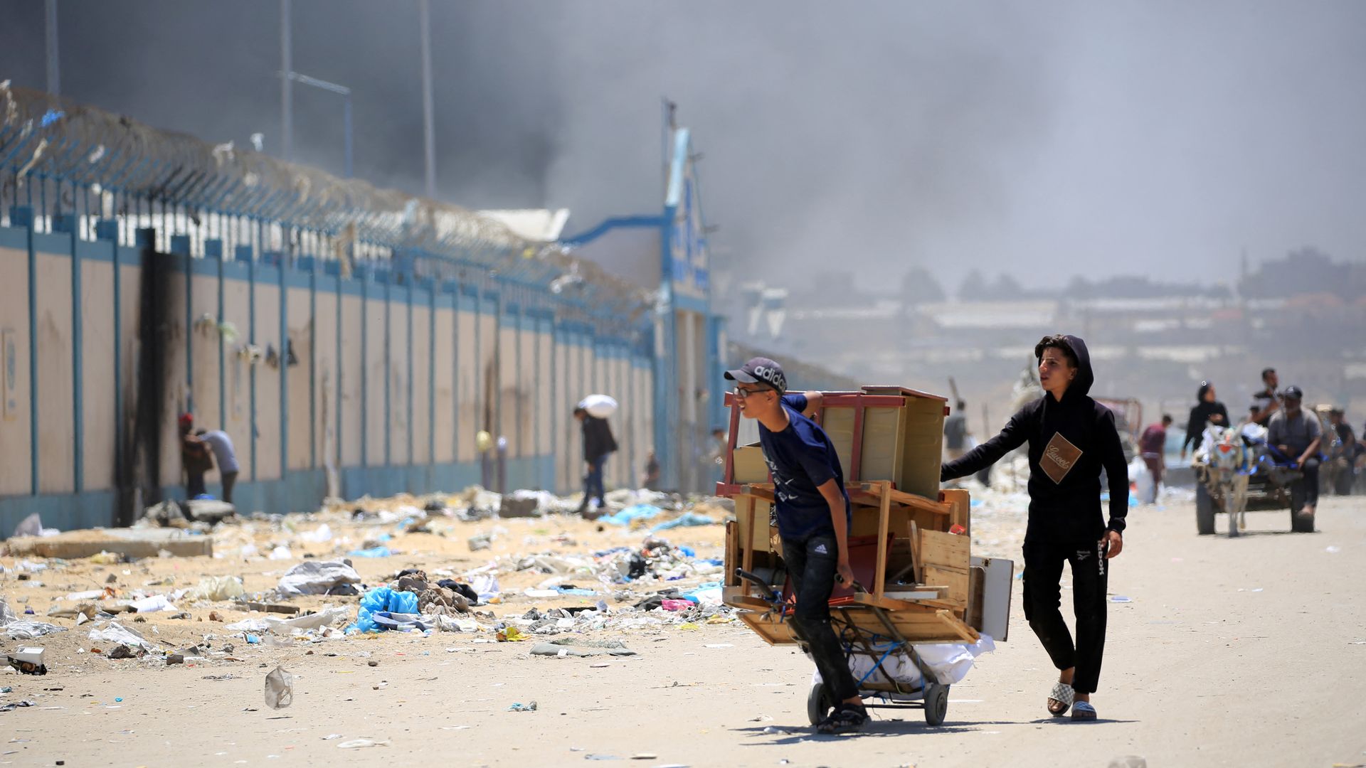 Palestinians flee with their belongings as smoke rises in the background, in the area of Tel al-Sultan in Rafah in the southern Gaza Strip on May 30, 2024