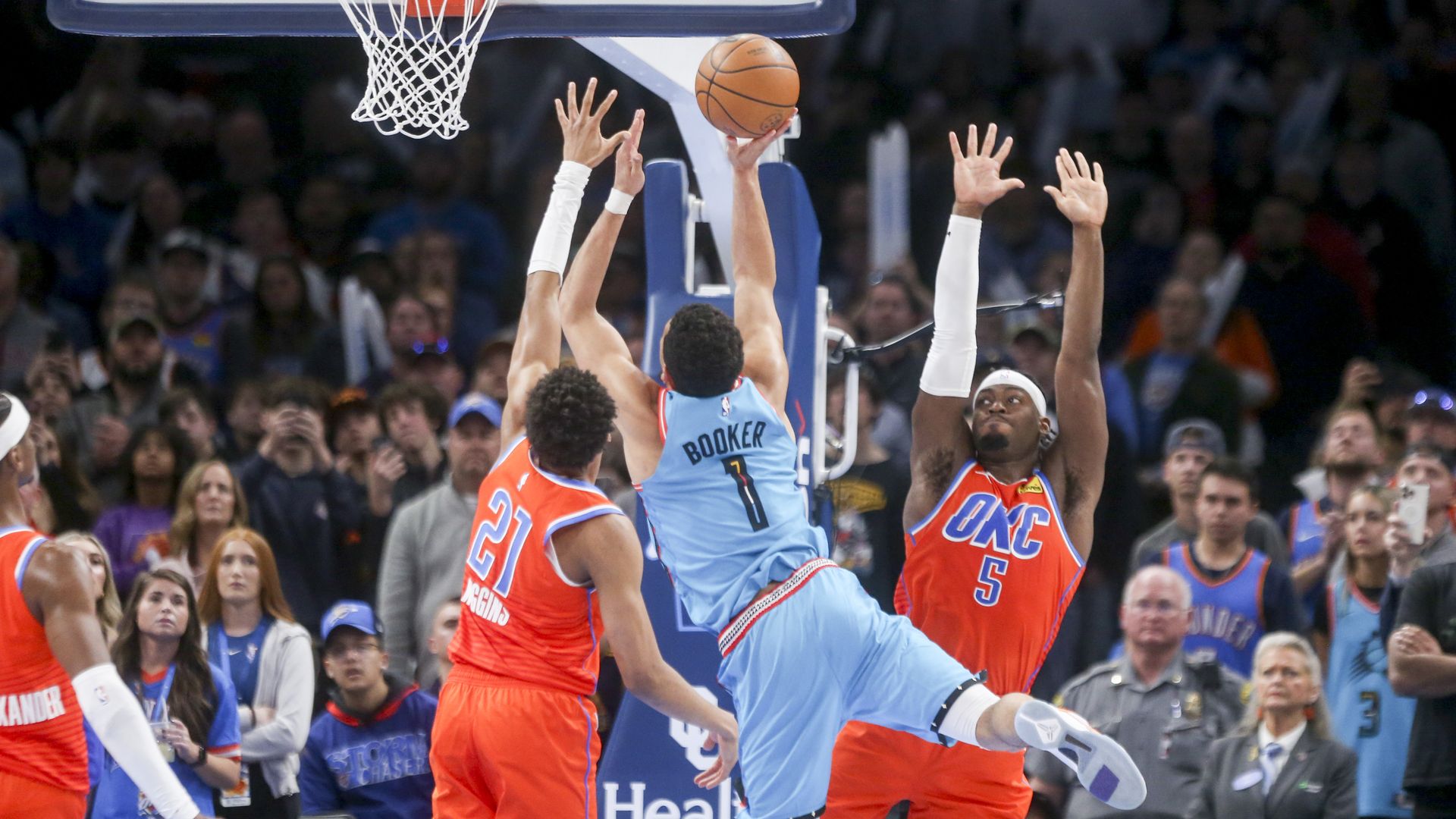 A view from behind as a basketball player lays up the basketball while being guarded by two defenders.