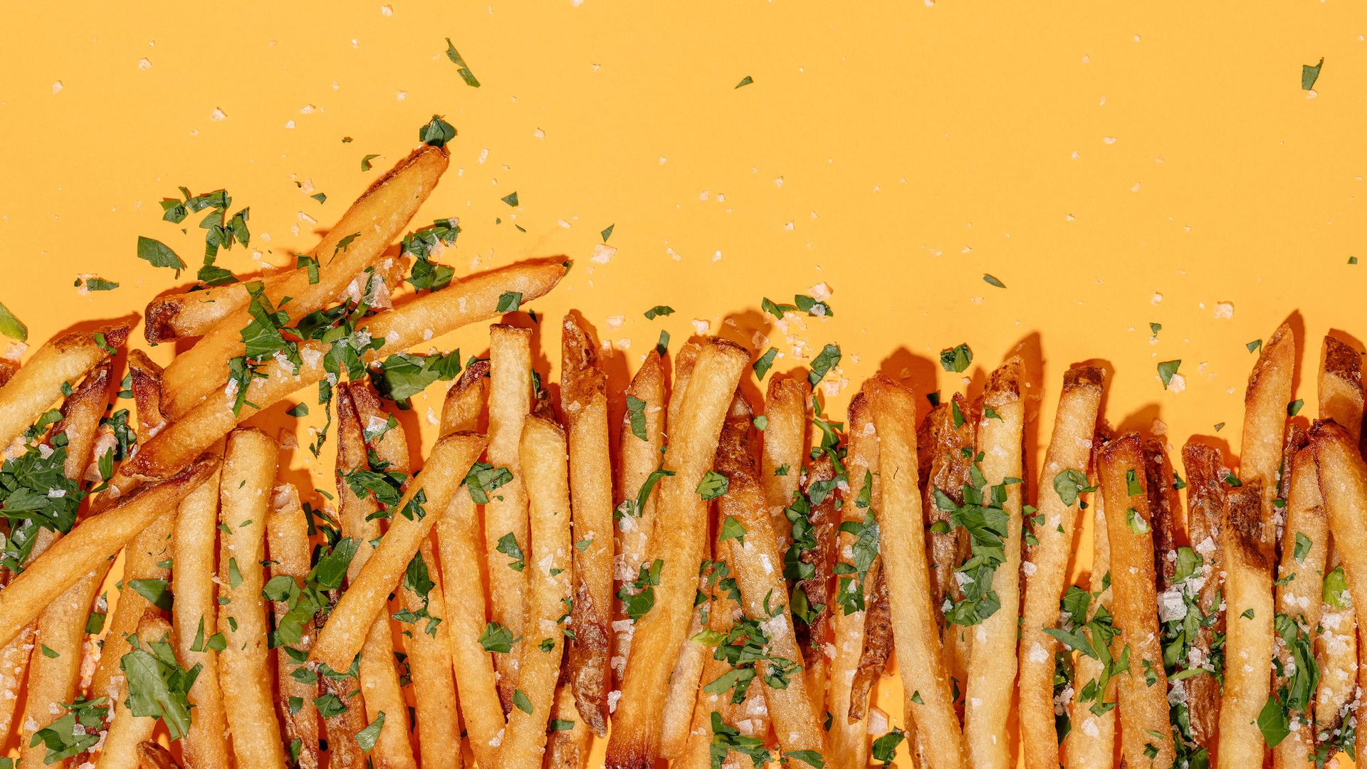 Jesse & Ben's beef tallow fries on a yellow background, dusted with parsley and salt