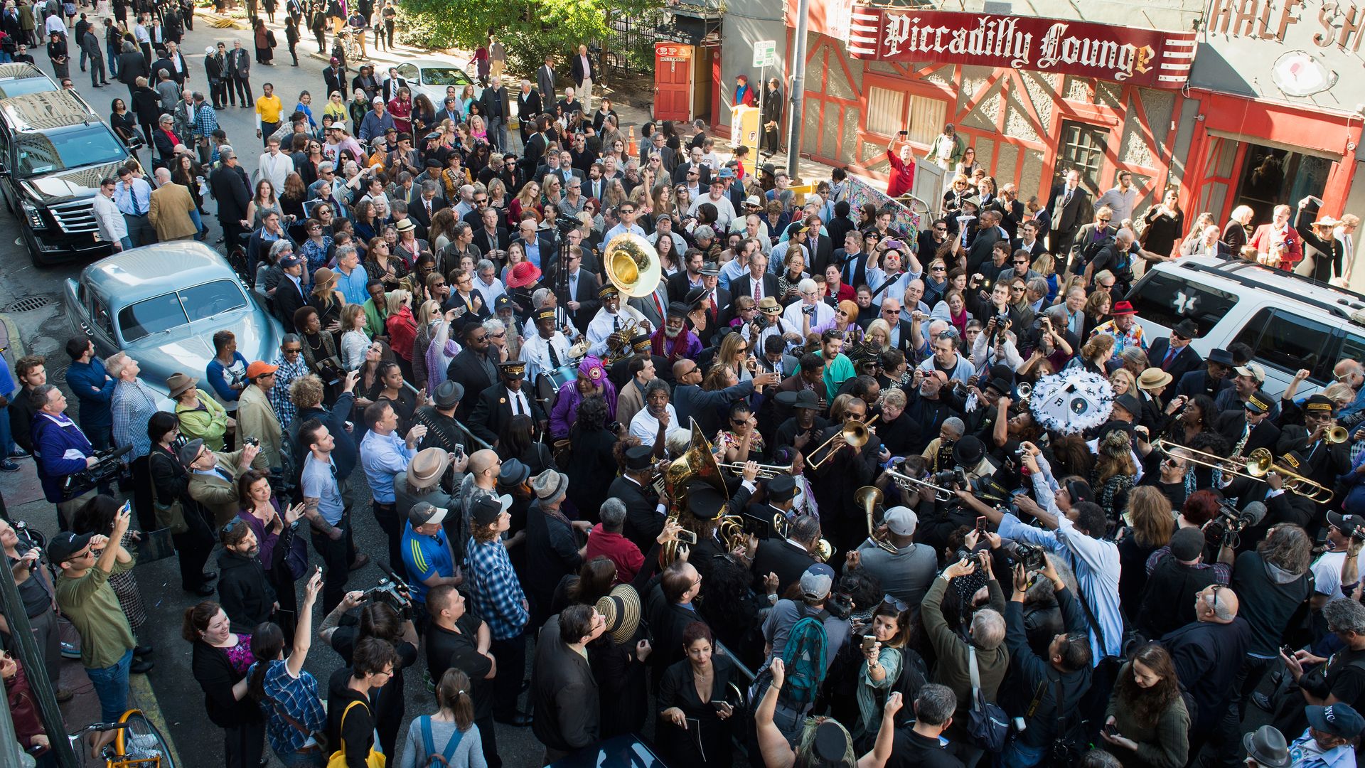 A large crowd of people, with musicians at the center, fills a New Orleans street.