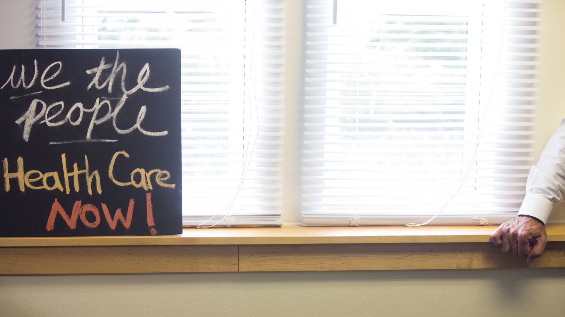 A sign that reads "We the people want healthcare now" sits on a windowsill