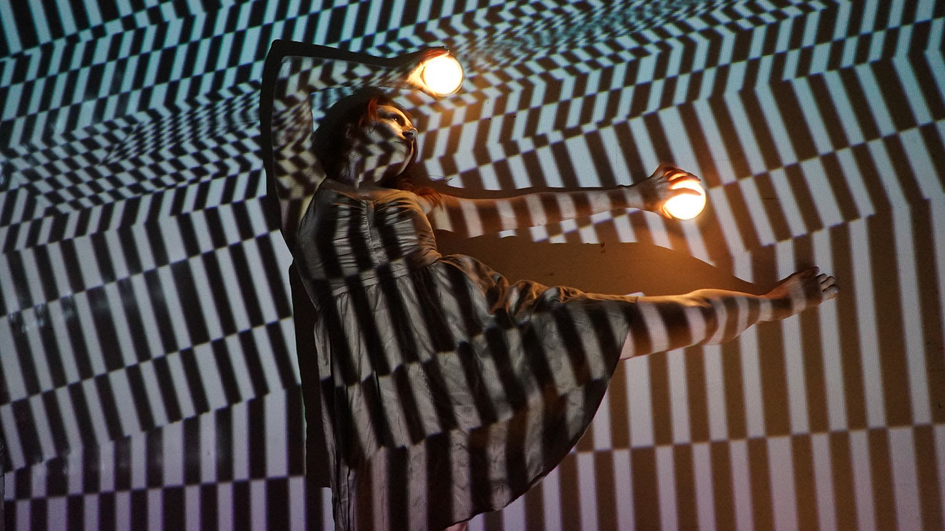 A woman holds two glowing bulbs while a warped checkered shadow is cast on her.