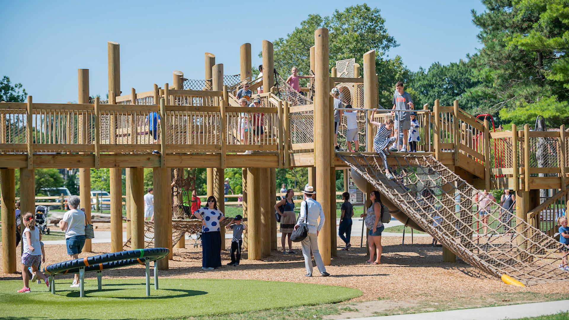 An elaborate wooden outdoor playground with children upon it.