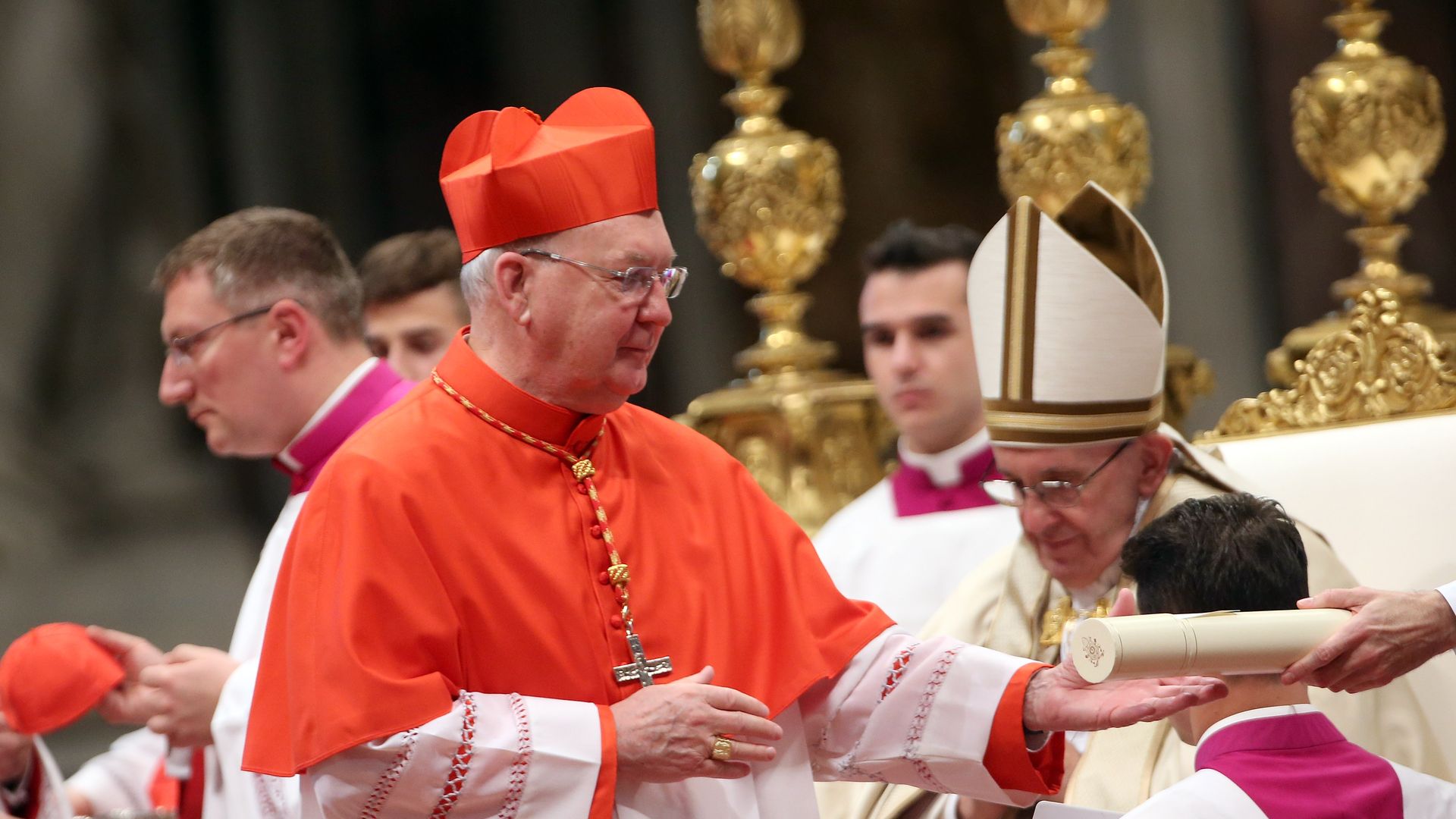 A man wearing white robe and red touches holds out his hand to take a scroll