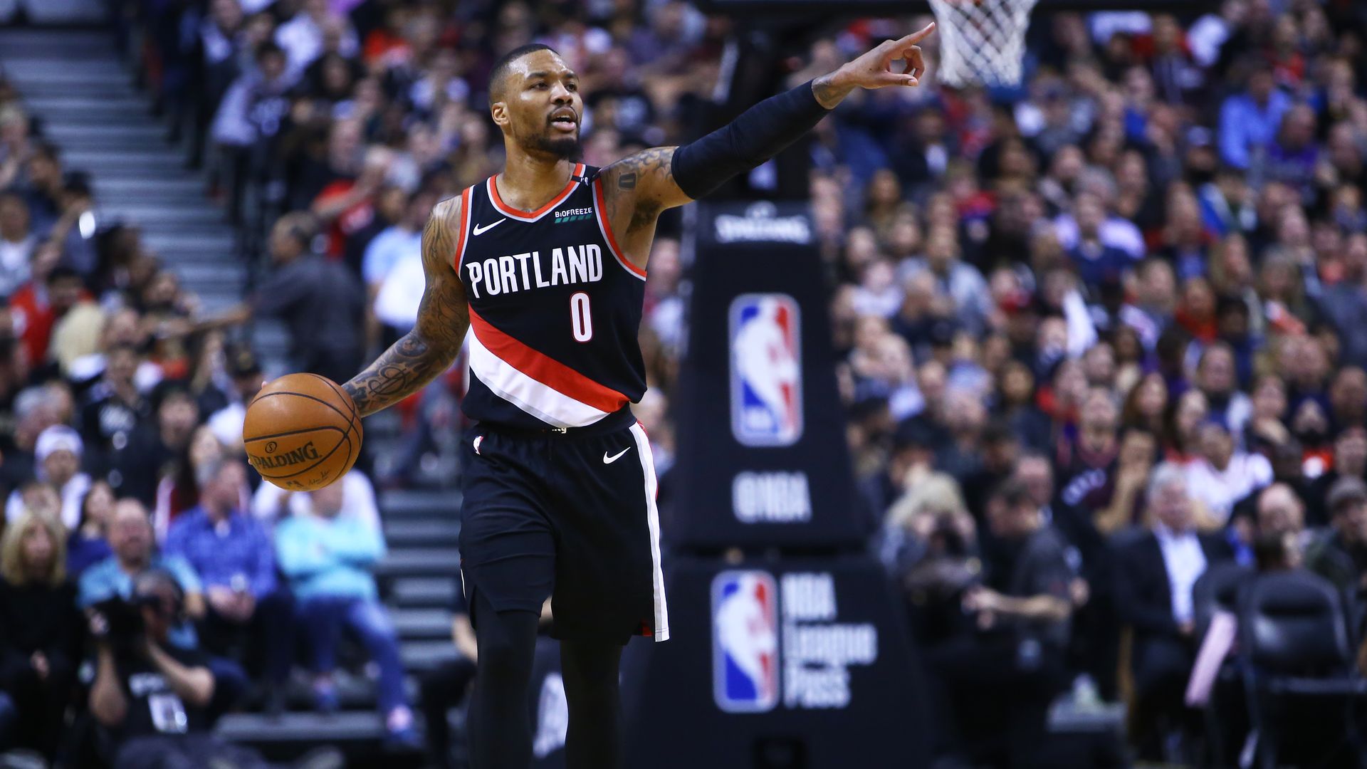Portland Trail Blazers player Damian dribbling a basketball and pointing on a basketball court with a crowd in the background.