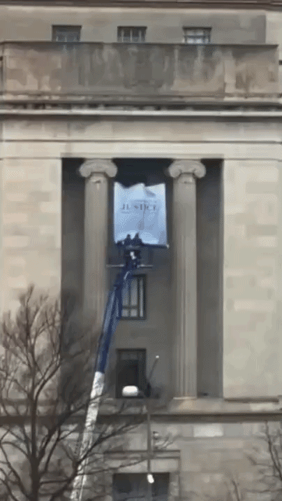 Construction works on a lift unfurl a banner of Donald Trump between two columns on the exterior of the DOJ building on Pennsylvania Avenue
