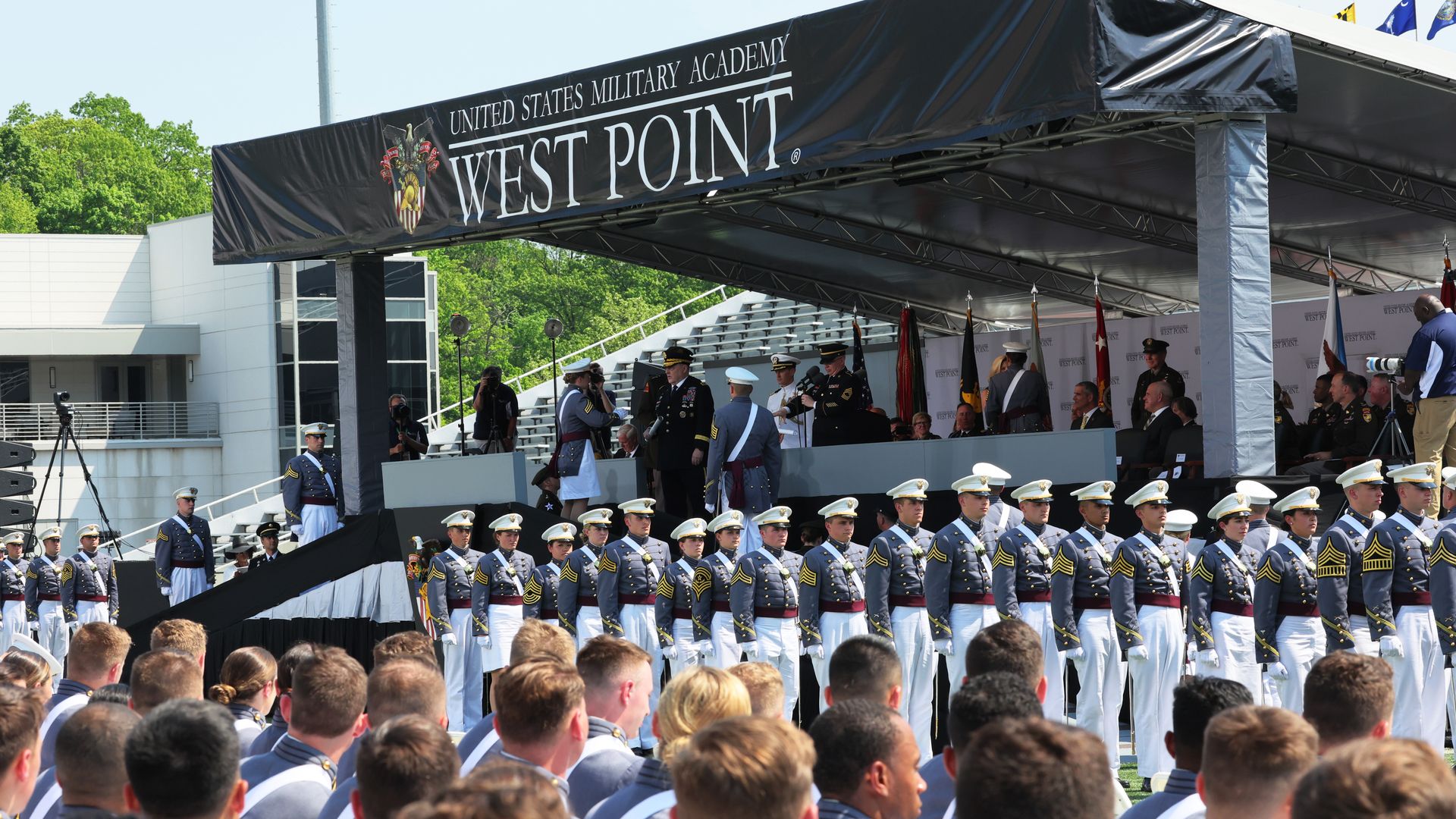 Graduates look at the stage at a commencement ceremony at the military academy. Dozens of people are in the foreground with a stage in the background. 