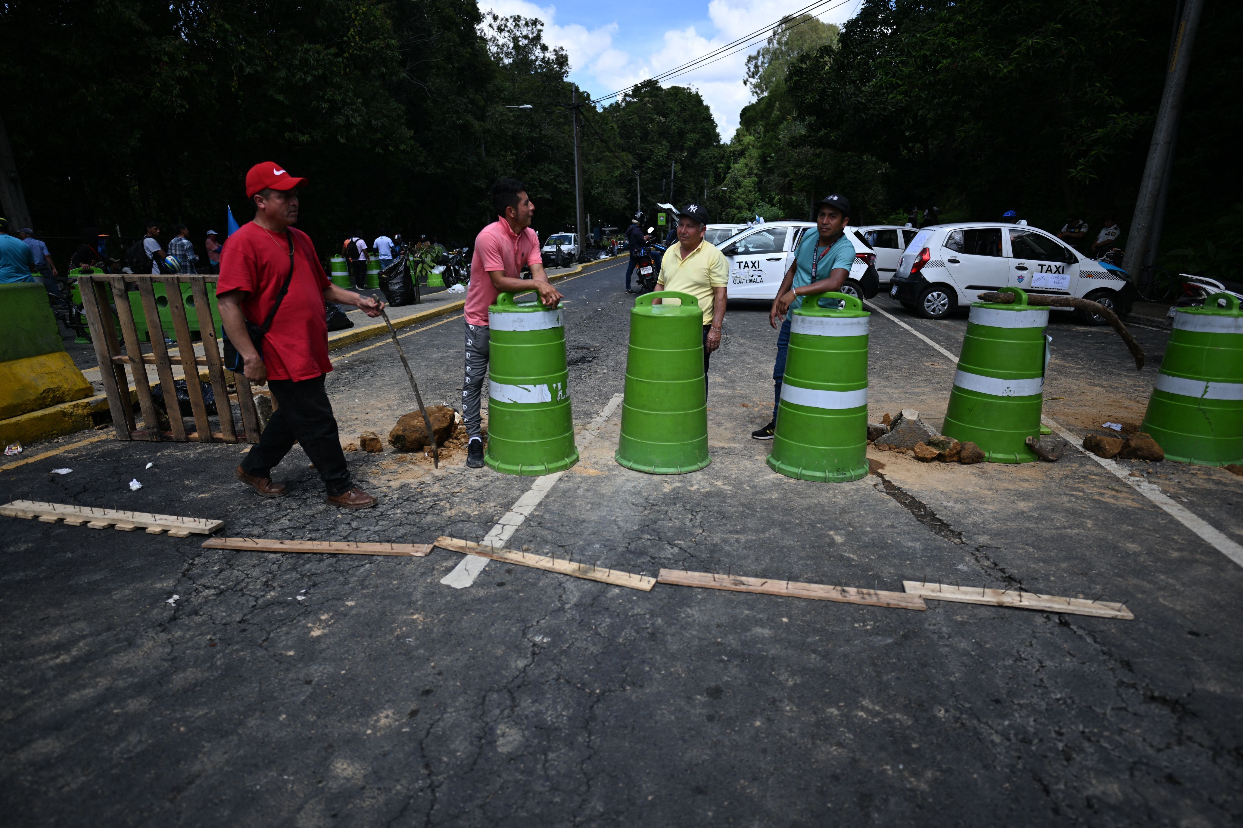Four men stand near several lime green barrels that are blocking access to a road in Guatemala City, Guatemala 