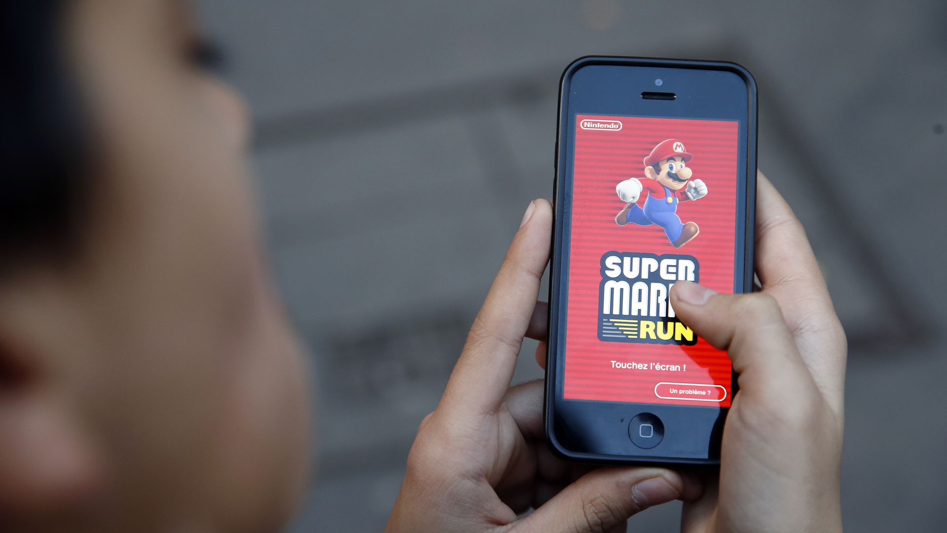 In this image, a woman holds a phone to the camera that displays the Mario Run game logo. 