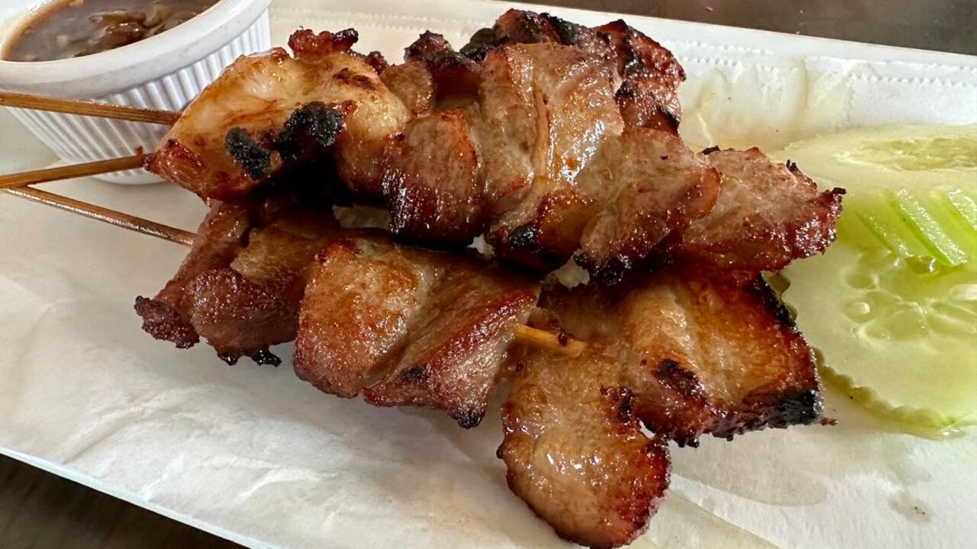 Photo shows cooked pork skewers on a plate with slices of raw cucumbers