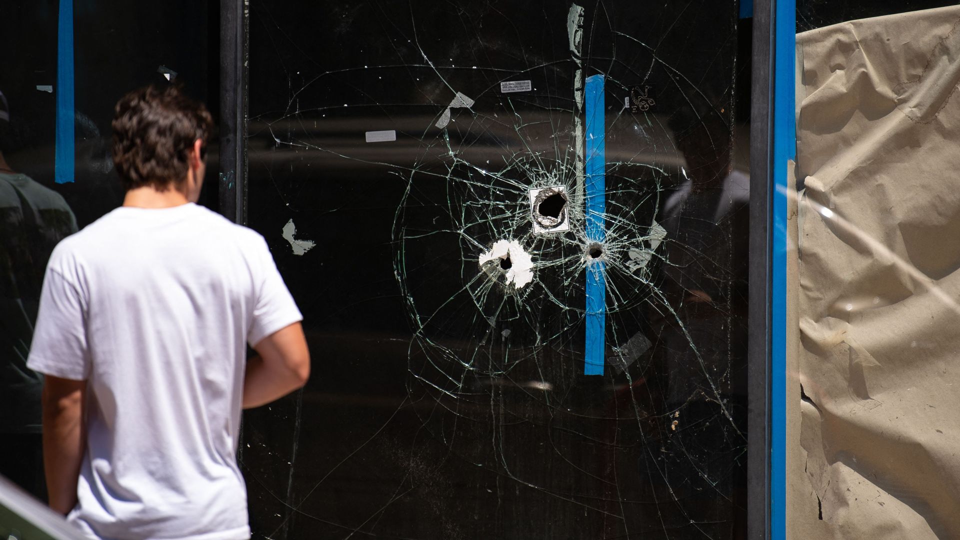 A pedestrian walks past bullet holes in the window of a store front on South Street in Philadelphia