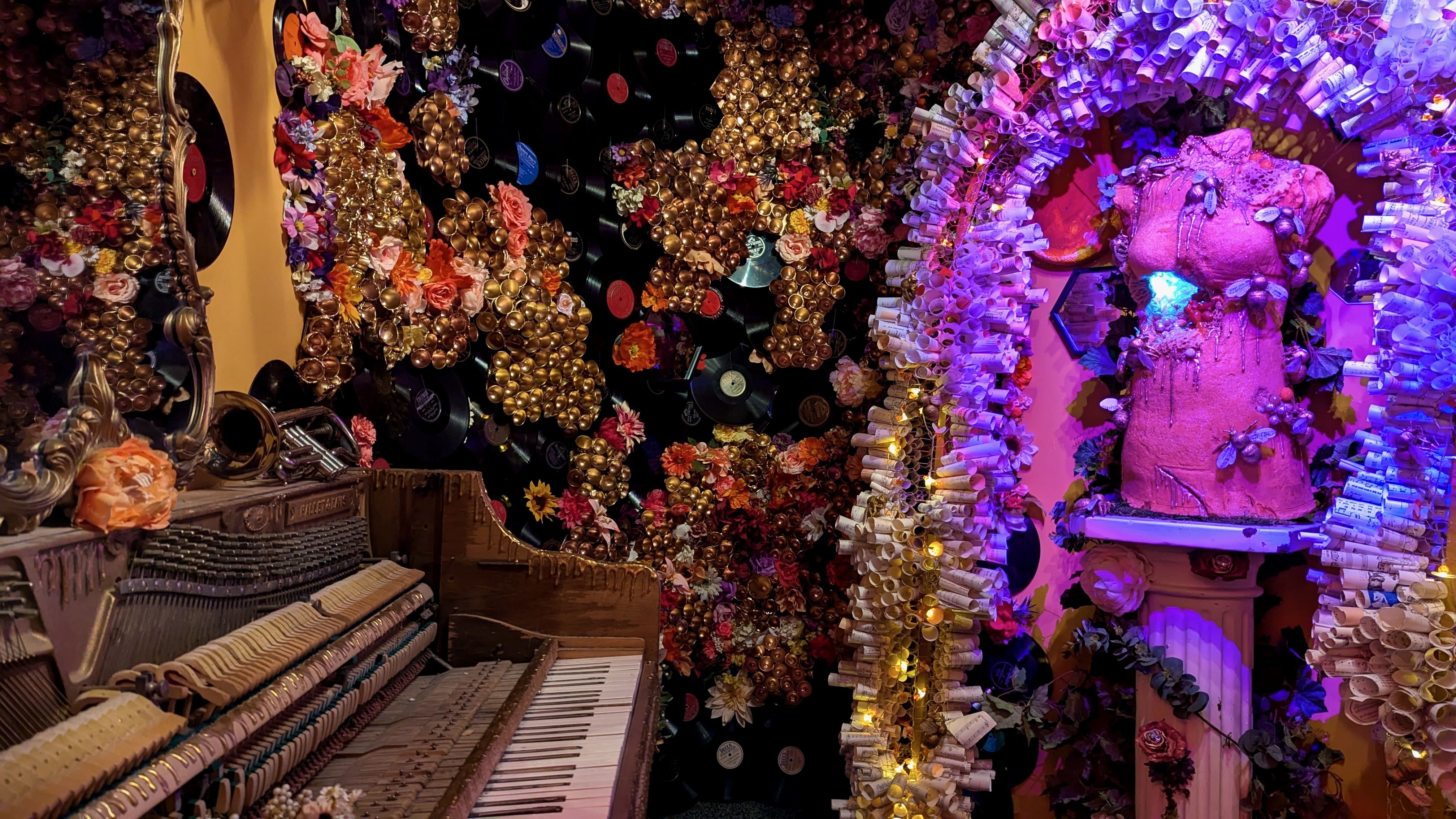 A piano and a manequin bust with glittering decorations and rolled sheets of music surrounding the bust