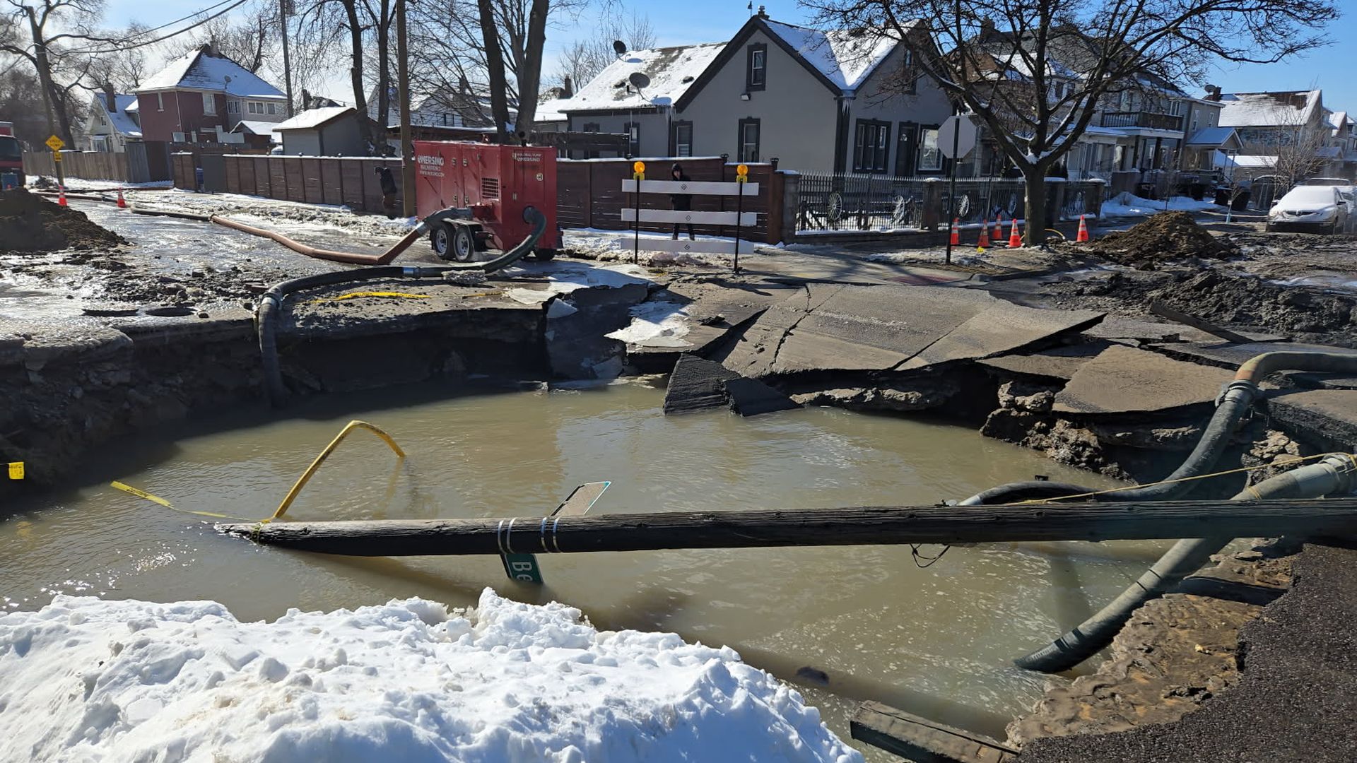 A hole with water is shown being pumped with houses behind.