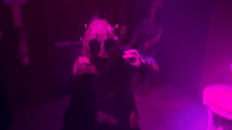 Video zooms in an out on a man in a mask that looks like a voodoo doll with pins sticking out of its head.