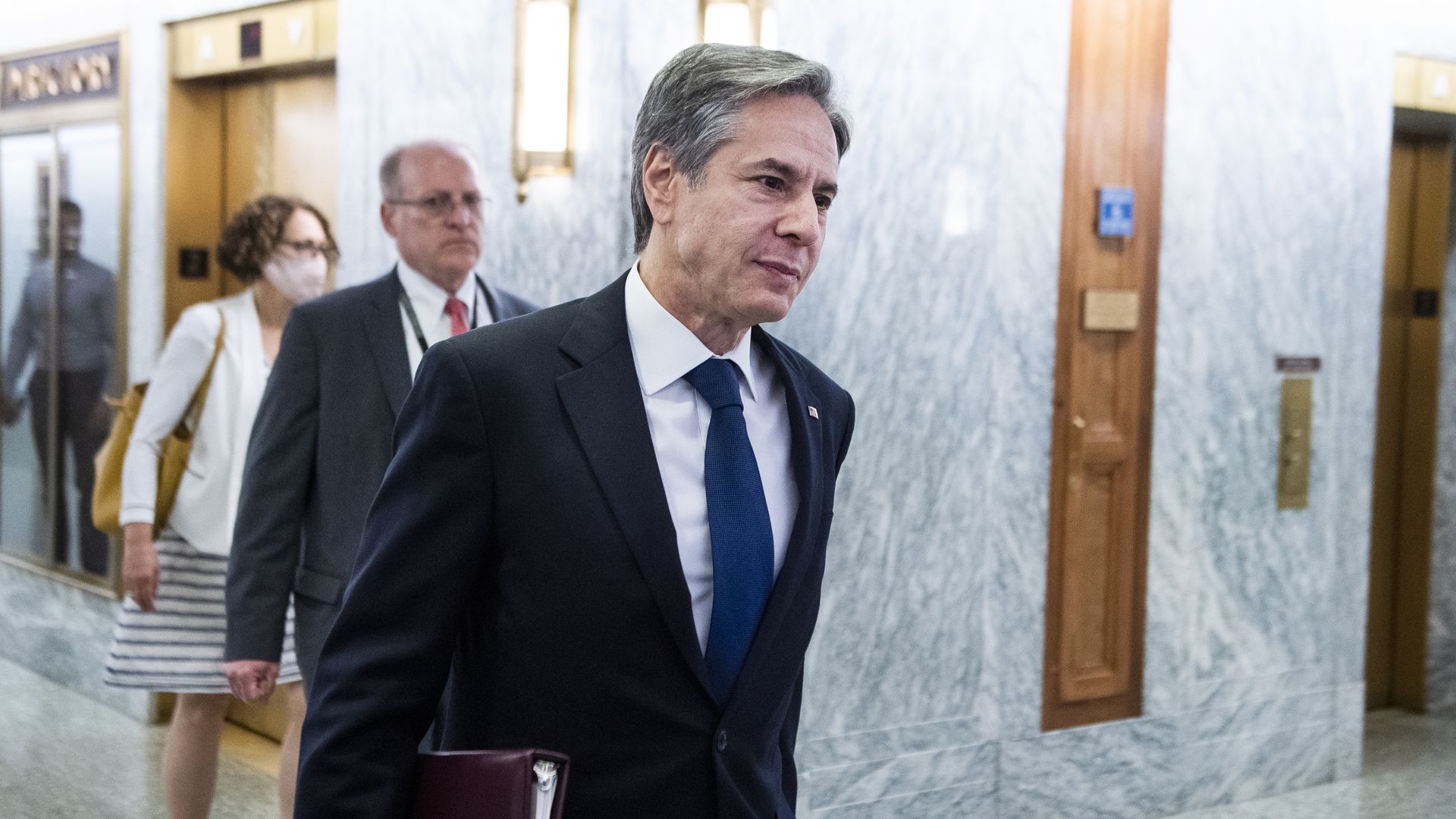 Photo of Antony Blinken walking in the halls of Congress with a folder under his arm