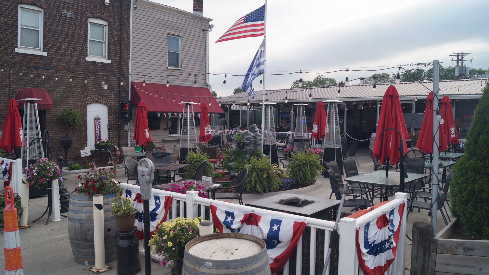 A patio during the day with closed umbrellas, bunting, trees, pub lights, etc. 