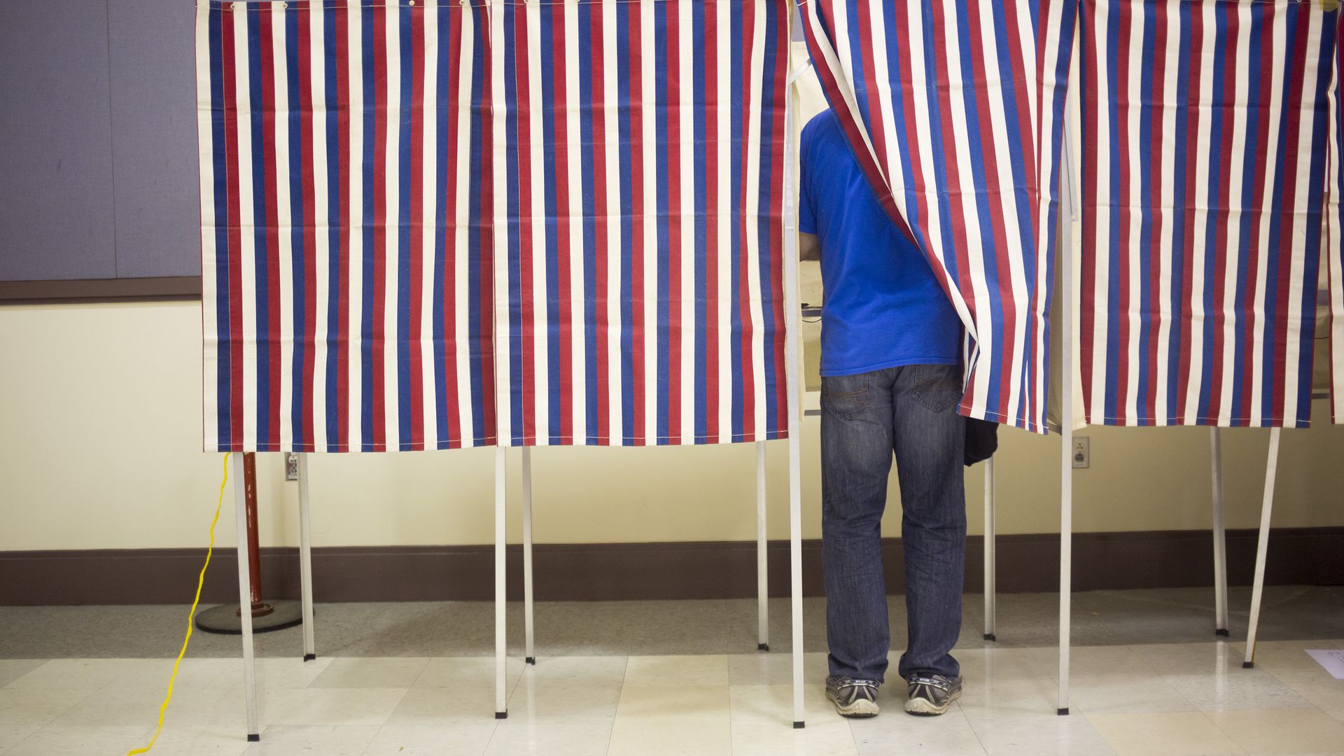 Red, white, and blue striped panels cover a voter voting in a polling booth.