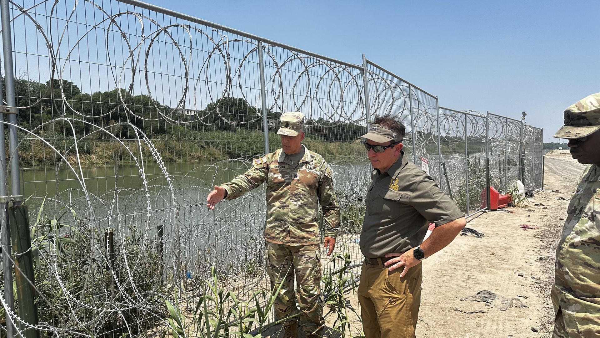 Jeff Landry observes a barbed wire-lined fence with a member of the US Army.