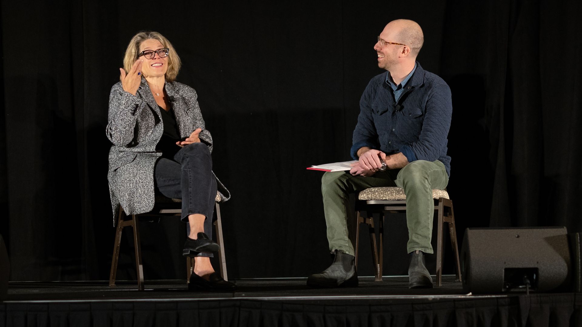 A photo of Engine Ventures CEO Katie Rae talking on-stage at a conference with Axios reporter Alan Neuhauser. Both are seated in chairs, with a black backdrop behind them.