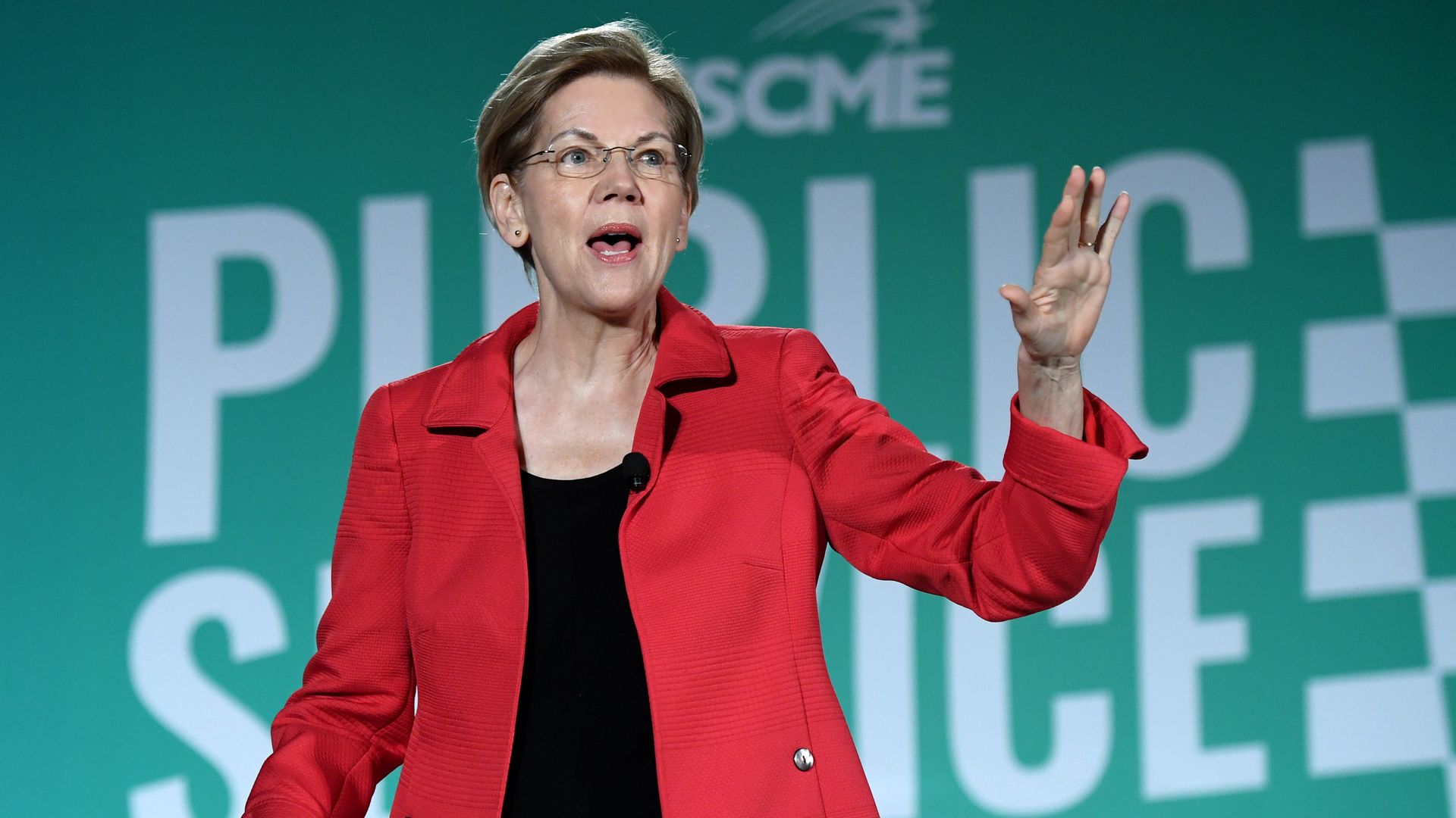 In this image, Warren wears a blazer and speaks on a stage.