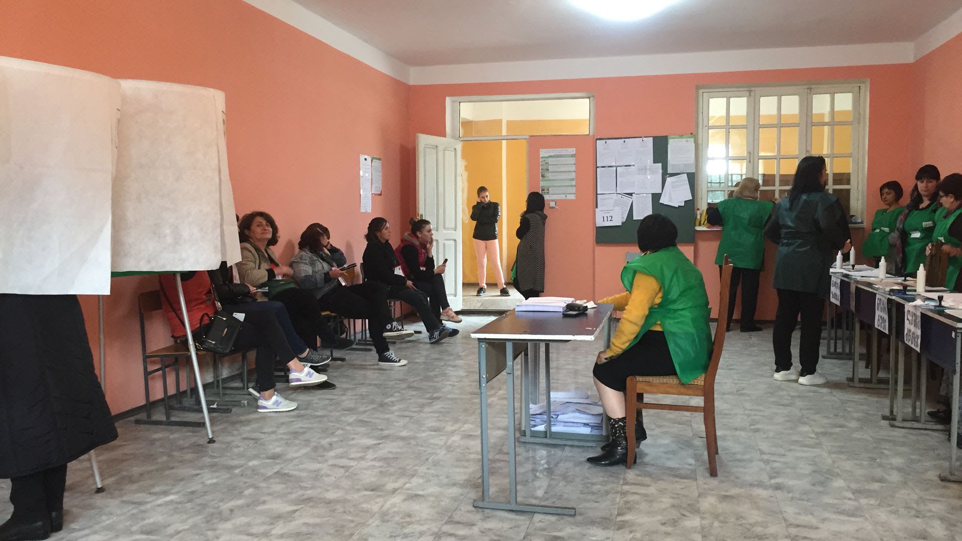 A man sits at a desk while people wait in seats in a small room at a polling station in Georgia