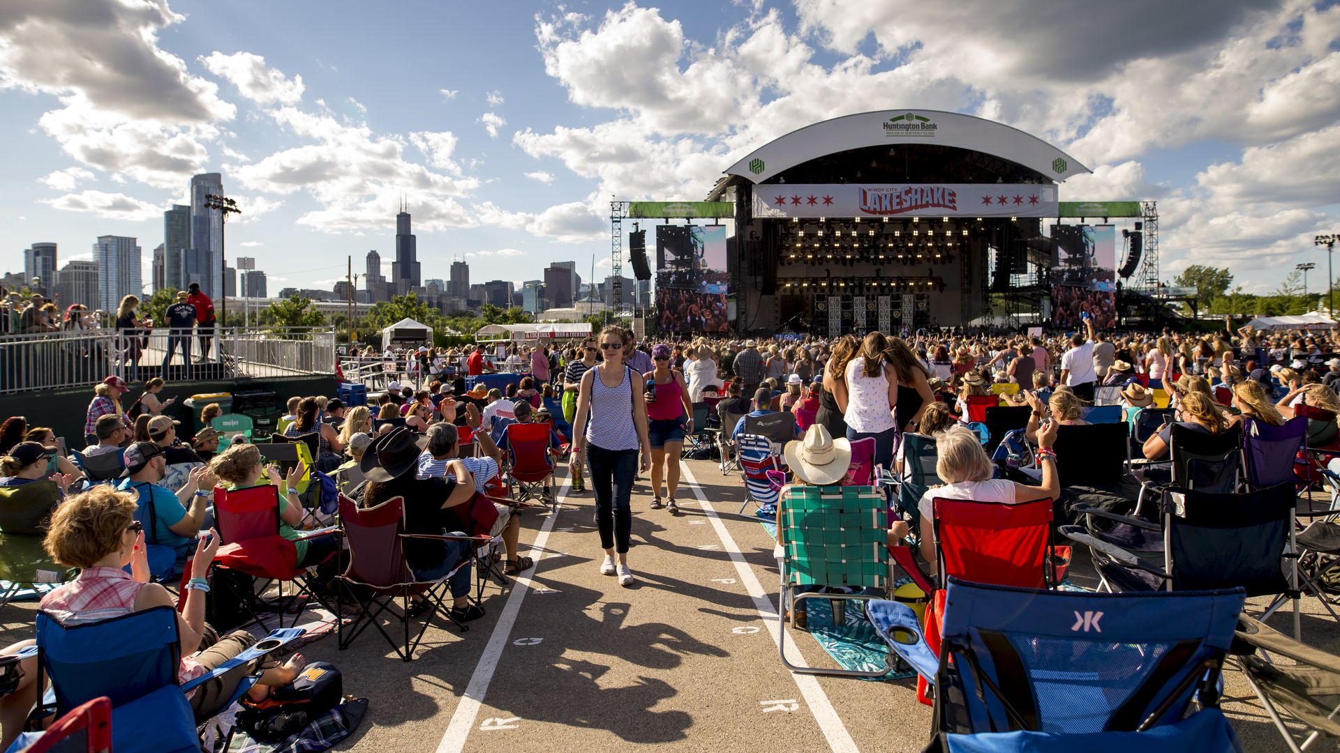 Seated crowds at outdoor concert with skyline in the background