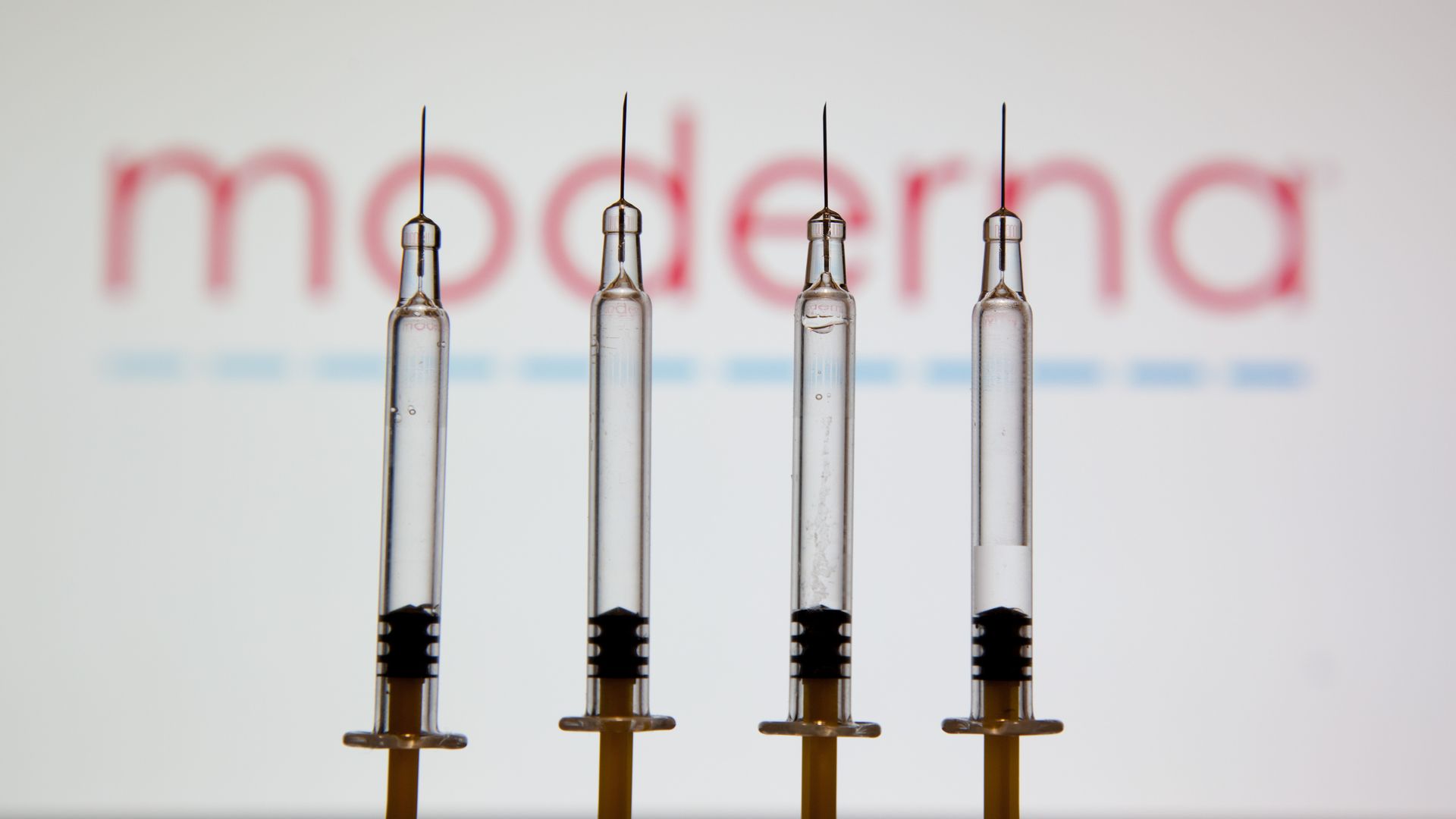 In this photo illustration, medical syringes seen displayed in front of the moderna's drug company logo