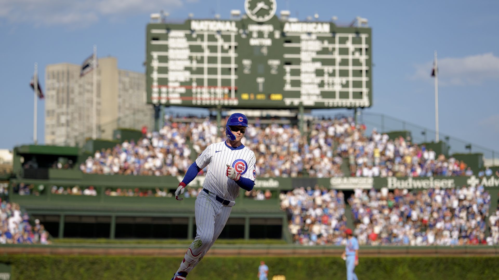 Photo of a baseball player rounding the bases with a old-time scoreboard and fans celebrating in background. 