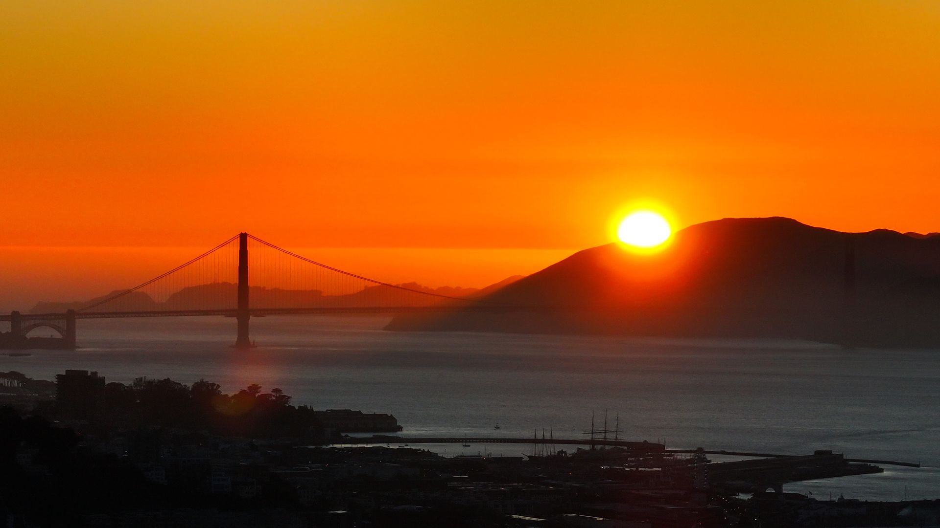 The sun sets behind a mountain with a silhouette of the Golden Gate Bridge