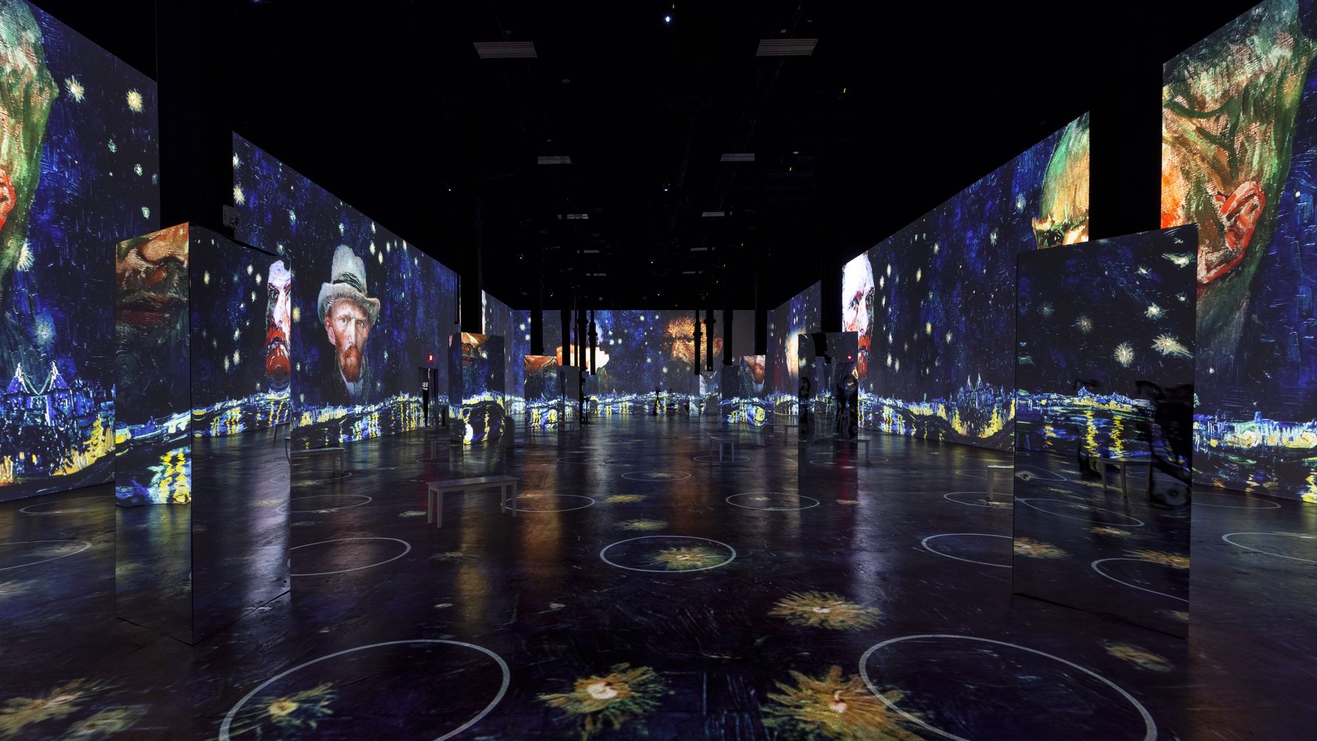 Silhouettes of people walk among projections of Vincent Van Gogh paintings on dark walls