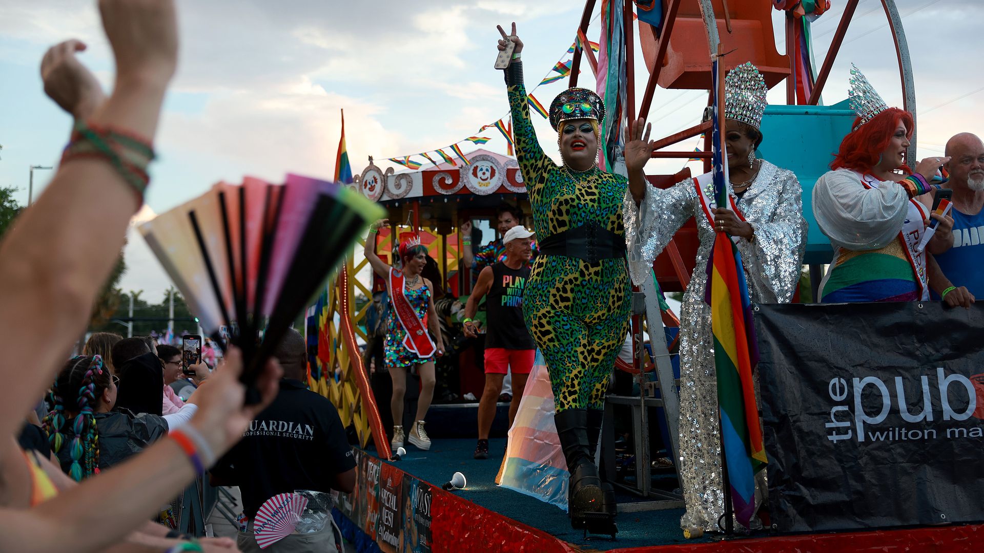A drag performer makes a peace sign from a float in a parade