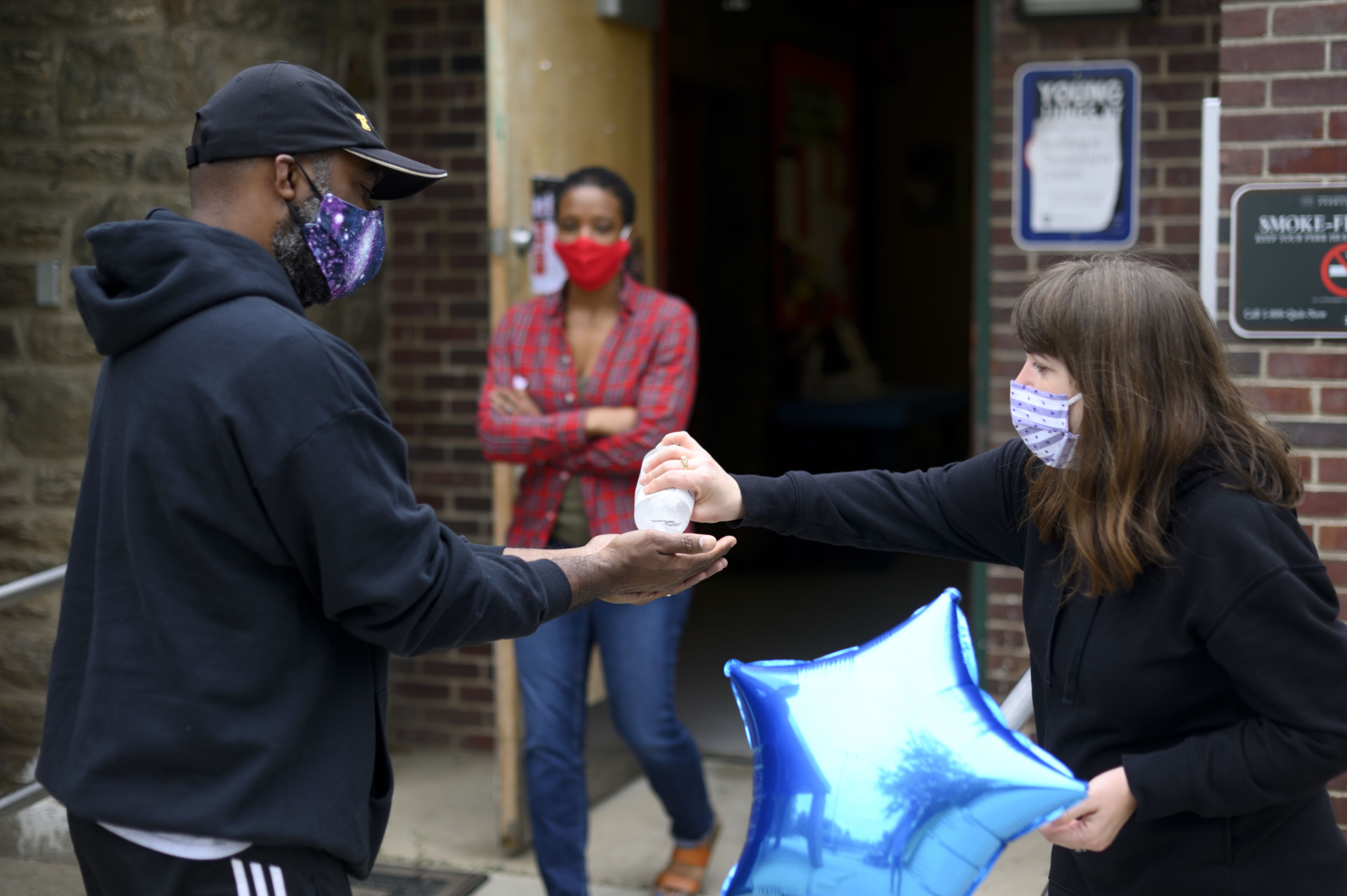 A woman offers hand sanitizer to a man wearing a face mask outside of an open doorway