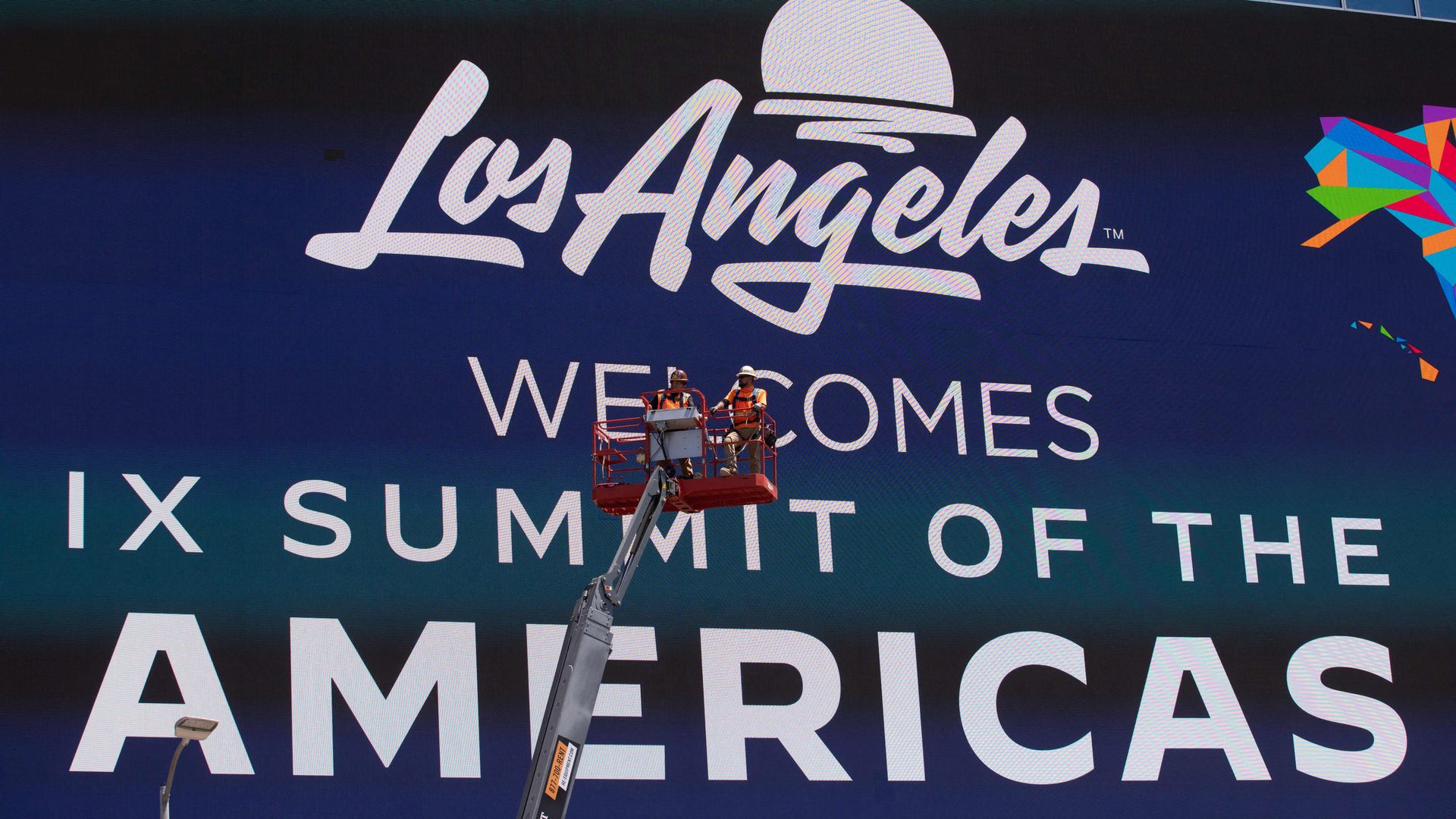 Workers adjust a large welcome ad for the Summit of the Americas