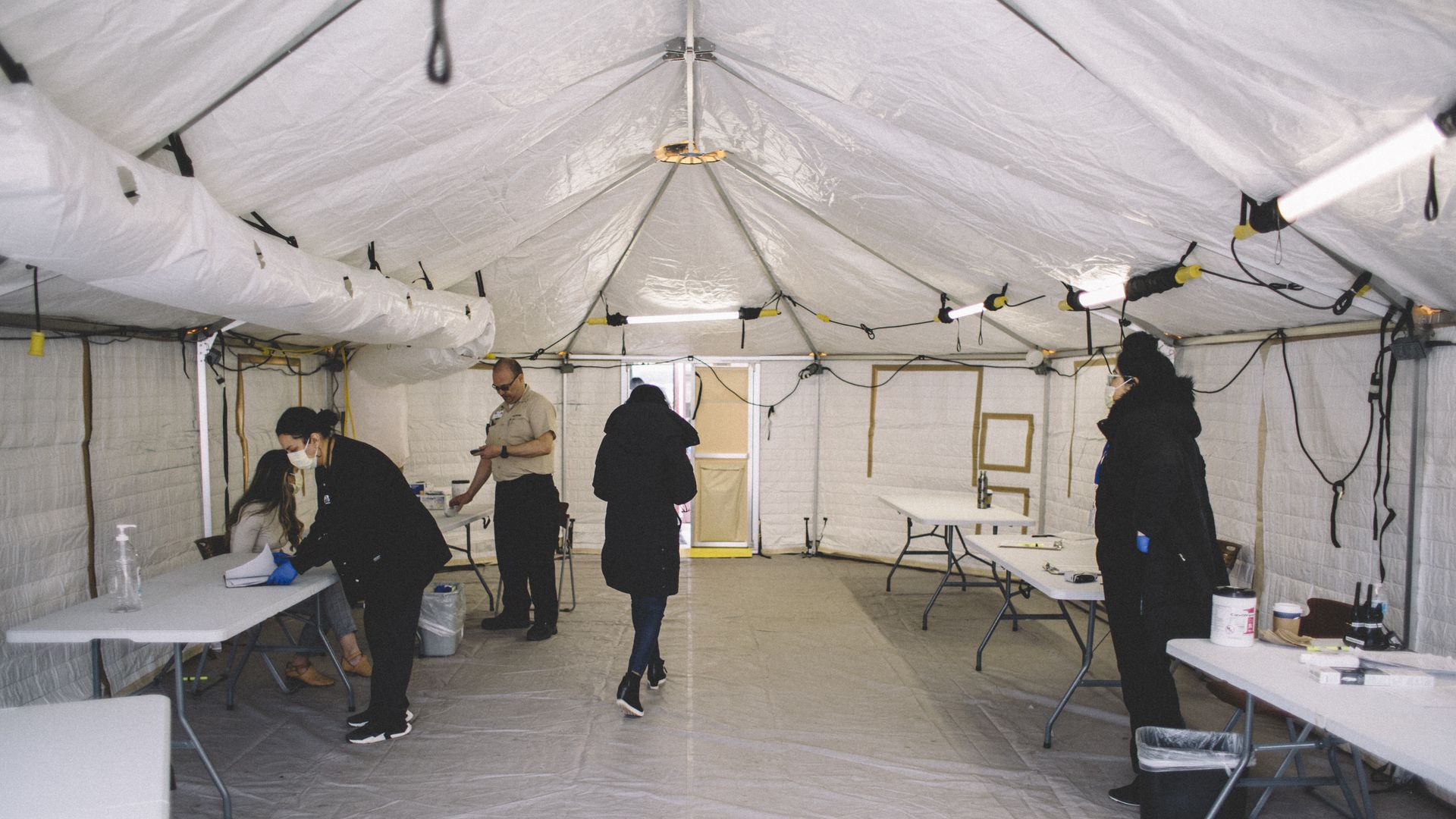 In this image, people stand in a white tent