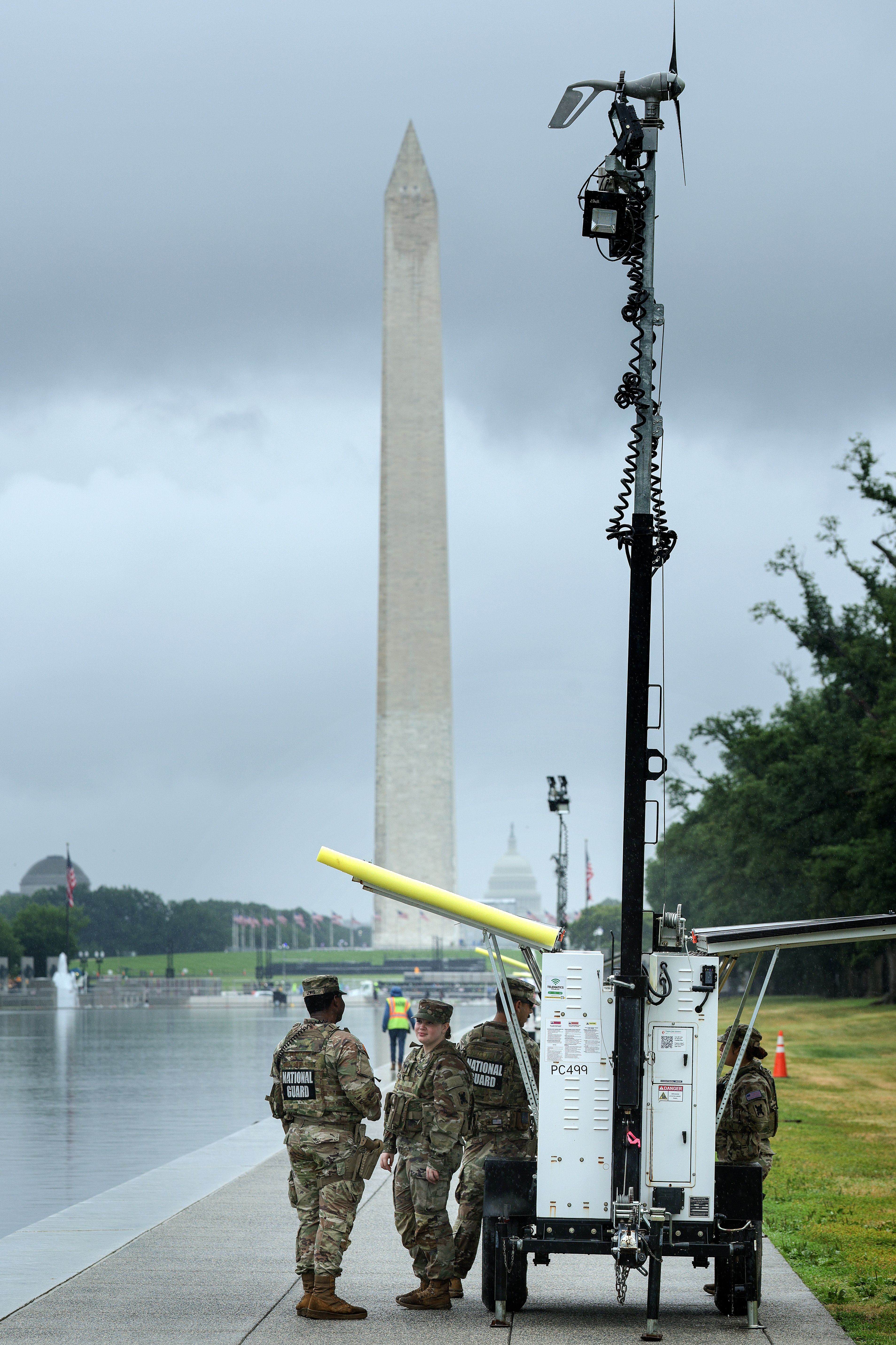U.S. Army National Guard troops take shelter from the rain underneath a mobile camera trailer's solar panels while guarding the Lincoln Memorial Reflecting Pool.