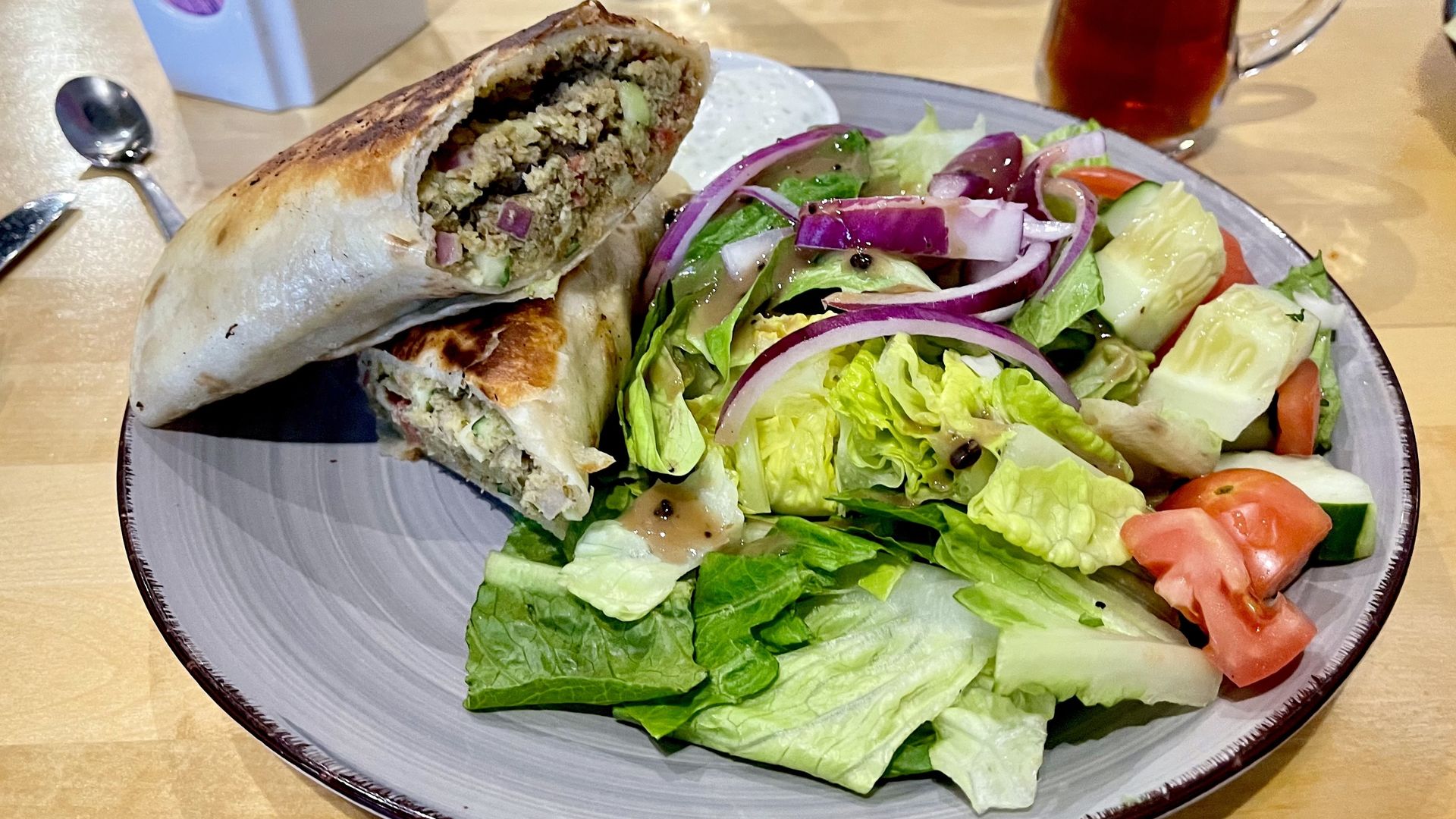 a falafel wrap stacked on a plate with a colorful salad next to a turkish tea