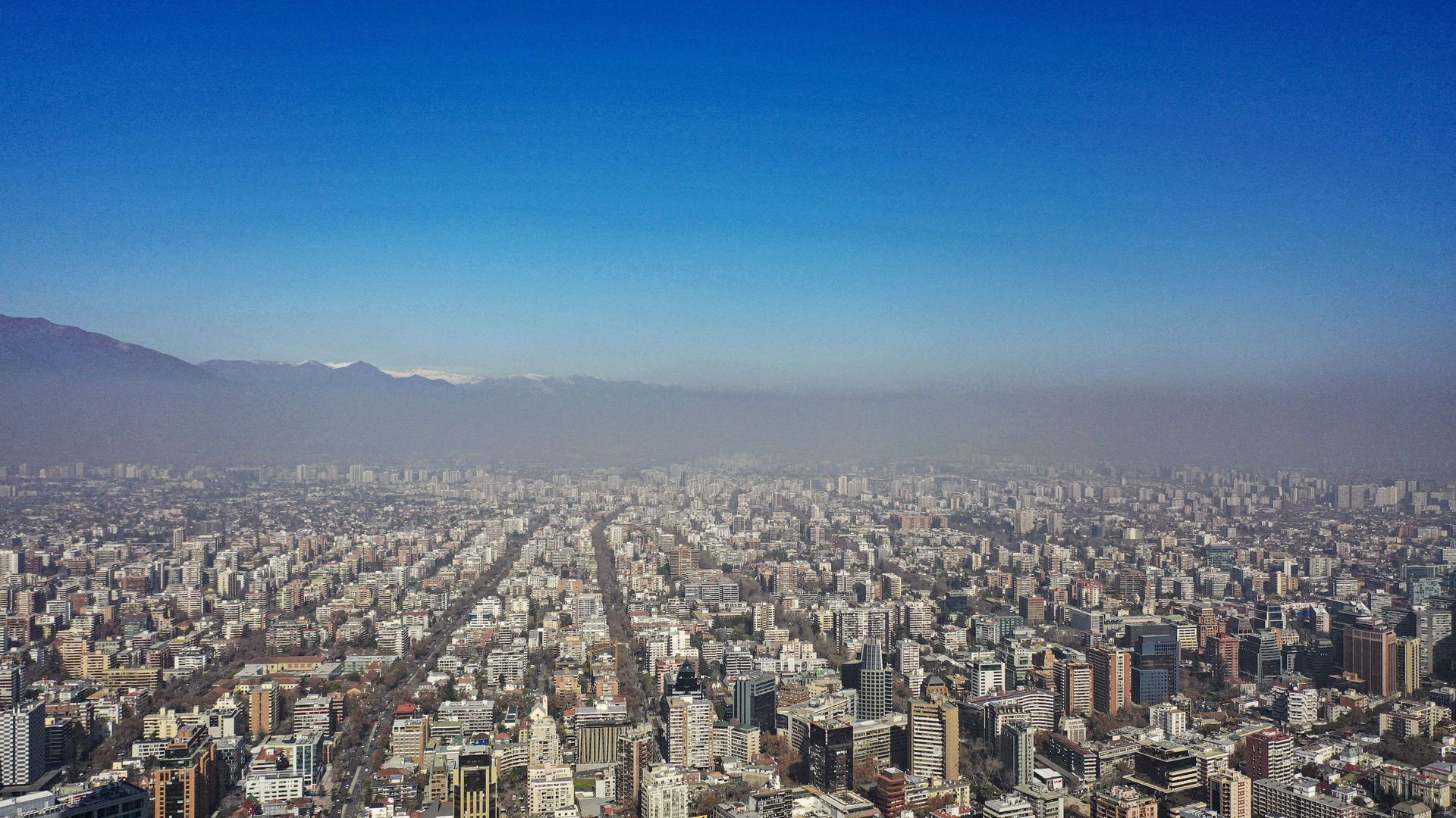 An aerial shot of Santiago, Chile, showing rows of buildings and mountains on the horizon with a dark cloud of smog above