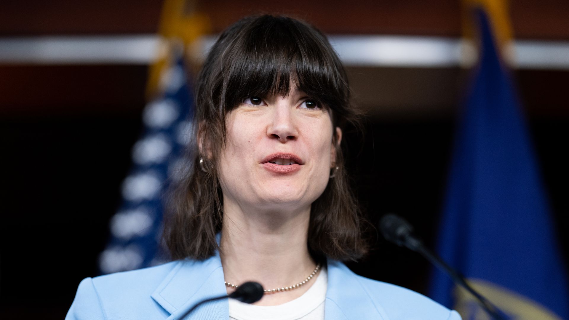 Marie Gluesenkamp Perez speaks into a microphone at a podium with flags visible in the background.