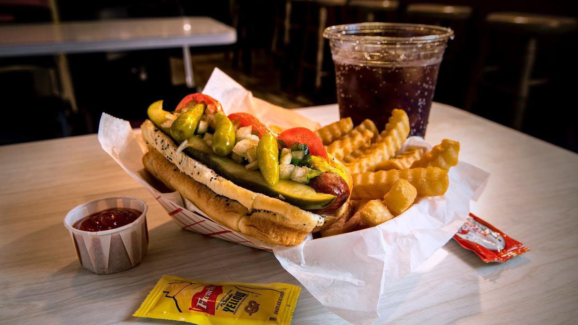 A hot dog and french fries with a Coca Cola in a plastic cup.