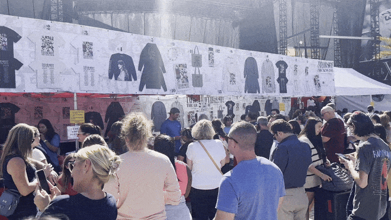 A camera pans across the sales tents of Taylor Swift merchandise as lines form.