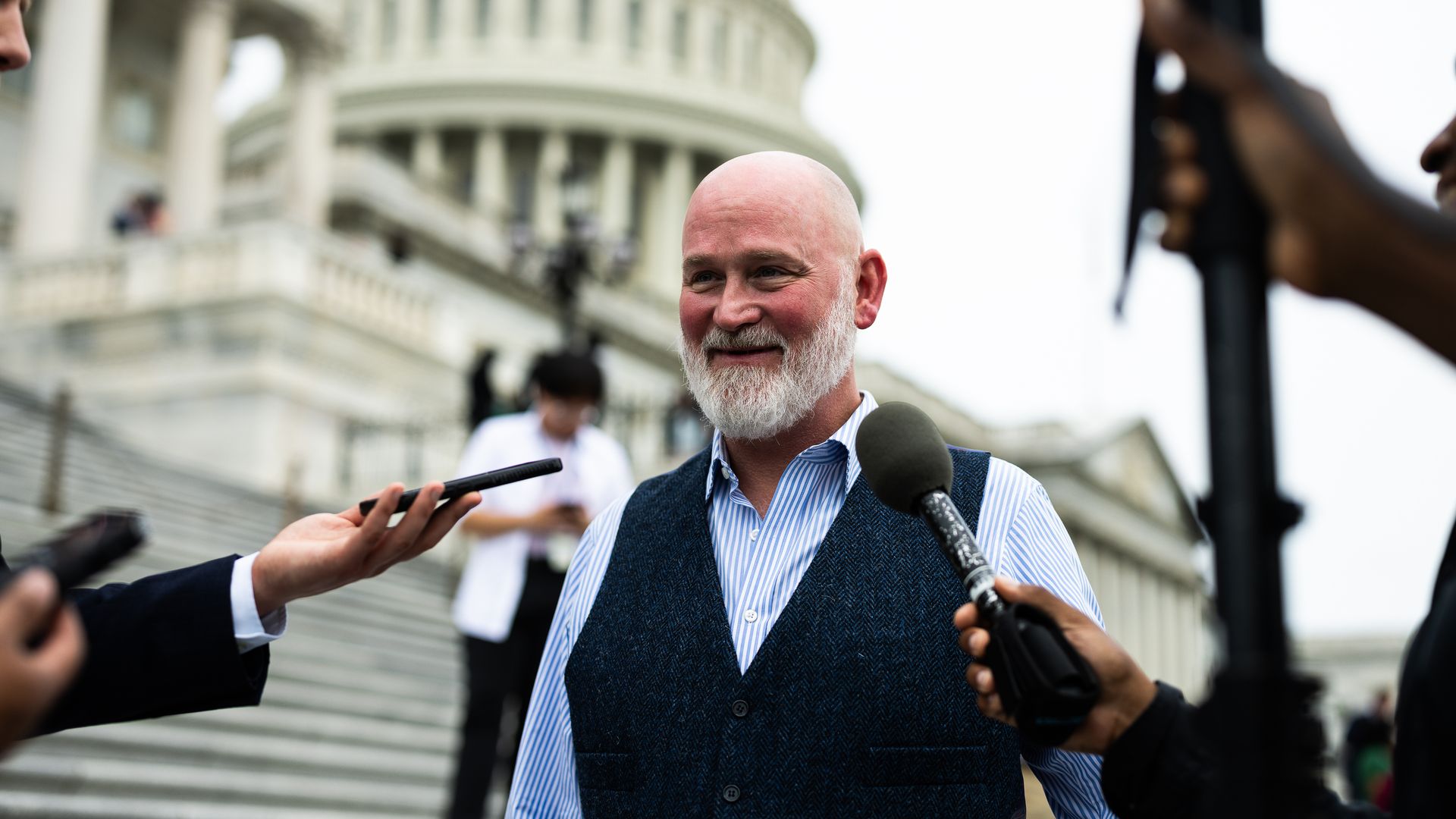 Rep. Derrick Van Orden wearing a blue shirt and dark blue vest, speaking to reporters outside the Capitol.