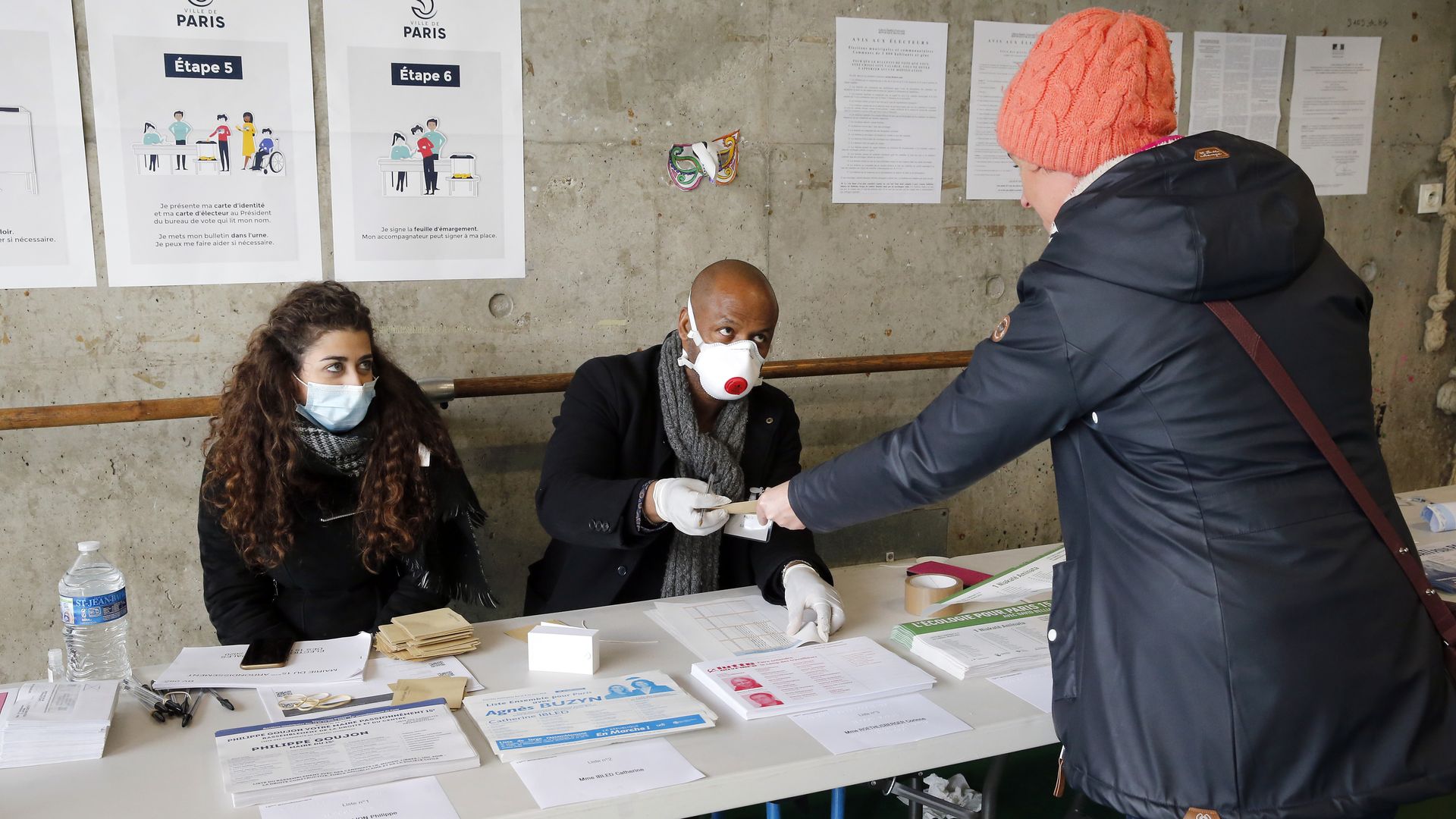 Electoral assessors wearing protective masks give a voting ballot.