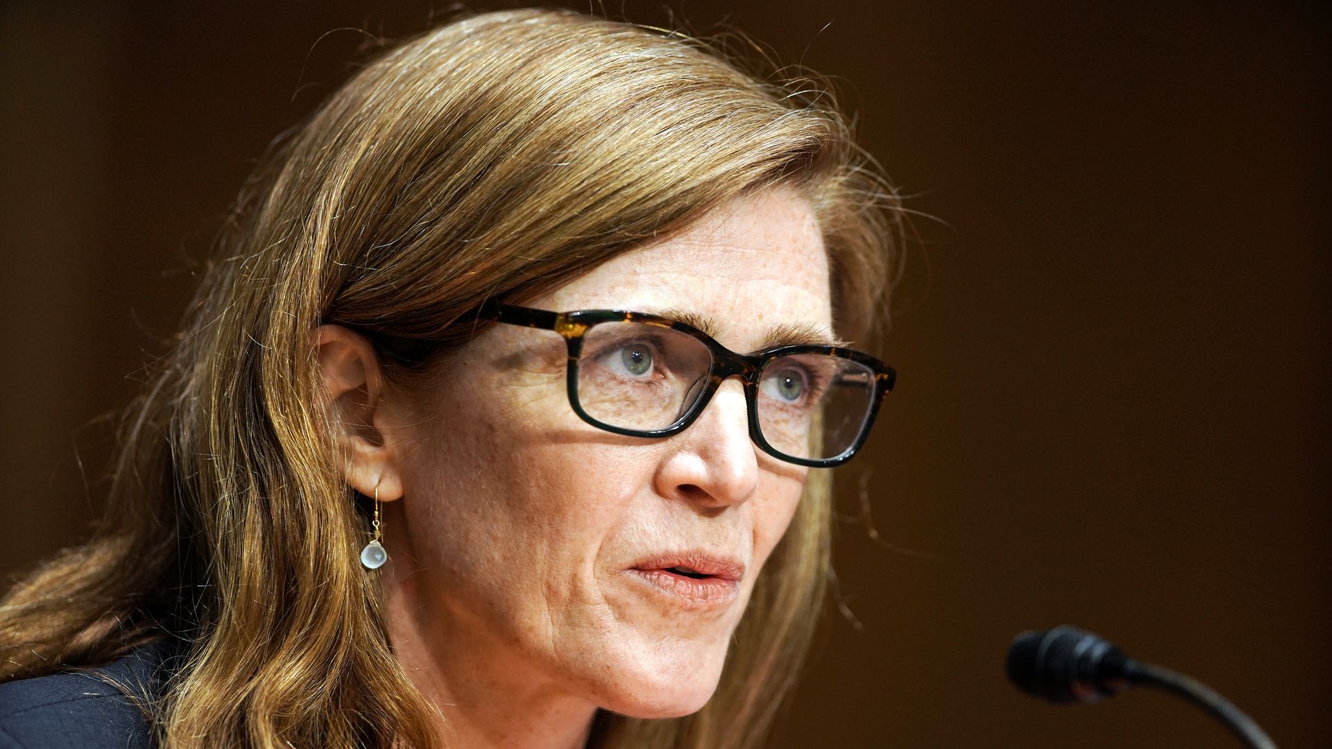 Samantha Power, wearing glasses, speaks into a microphone 