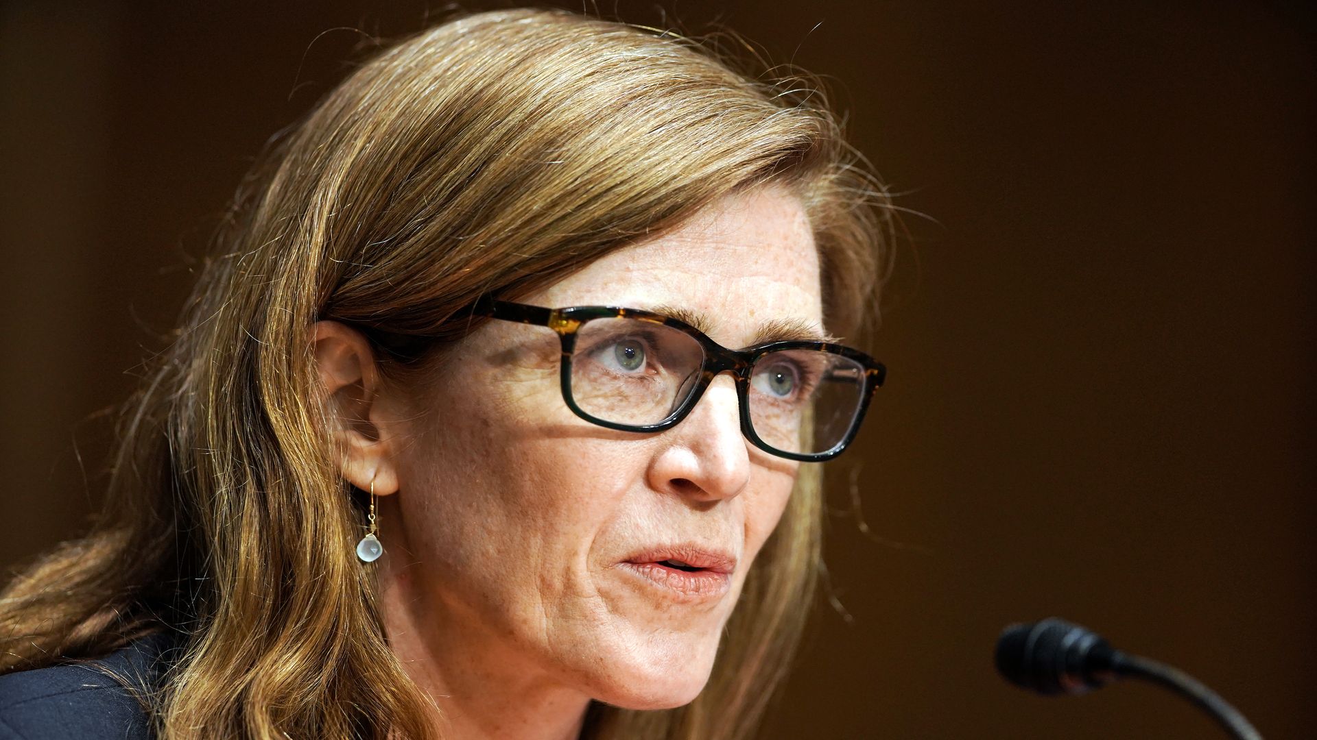 Samantha Power, wearing glasses, speaks into a microphone