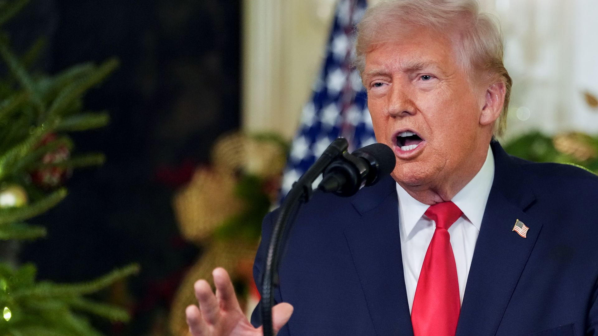 Trump, wearing a blue jacket, red tie and white shirt, speaks into a microphone.