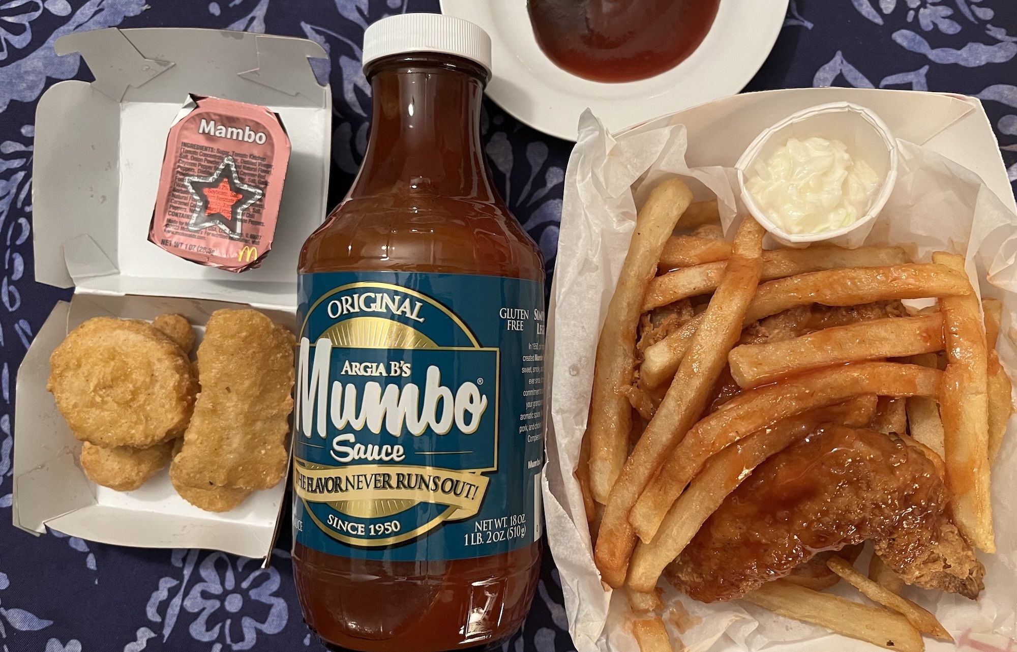 Chicken nuggets next to bottle of Mumbo sauce next to french fries and chicken wings.