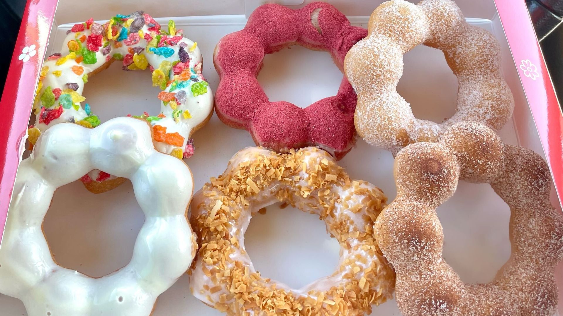 six colorful ring-shaped donuts in a white box