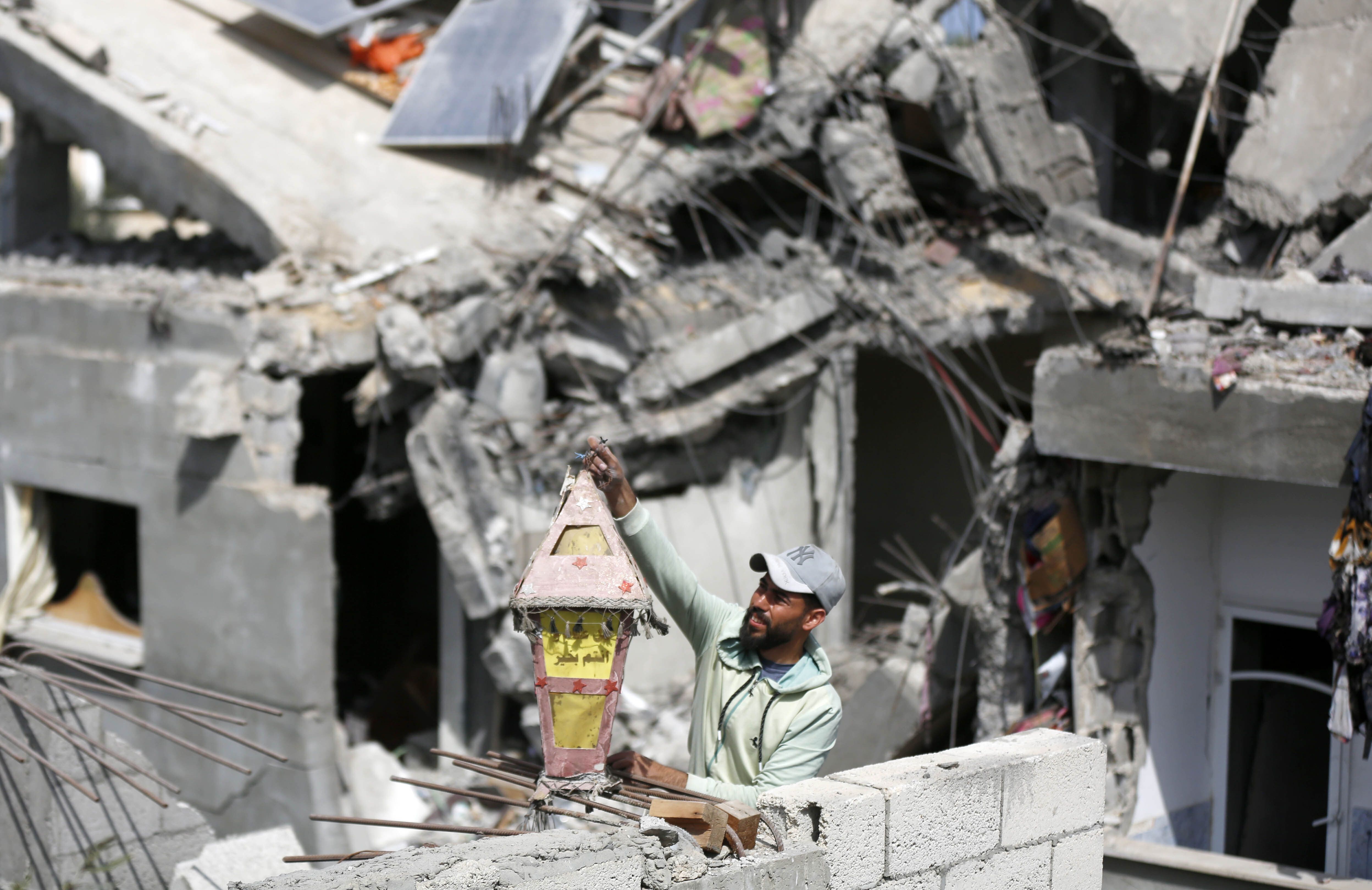 A man holds up a Ramadan lantern amidst the destruction of his home.  