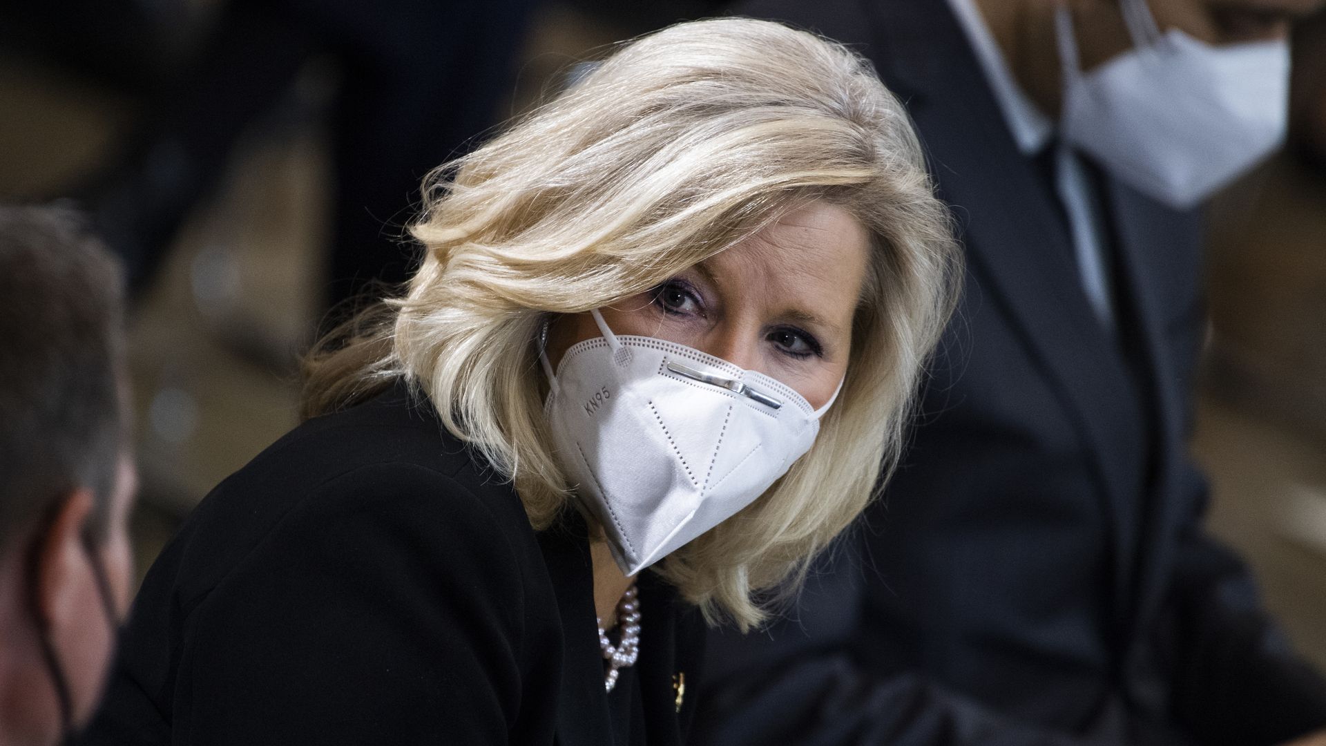 Photo of Liz Cheney wearing a mask and looking over at someone