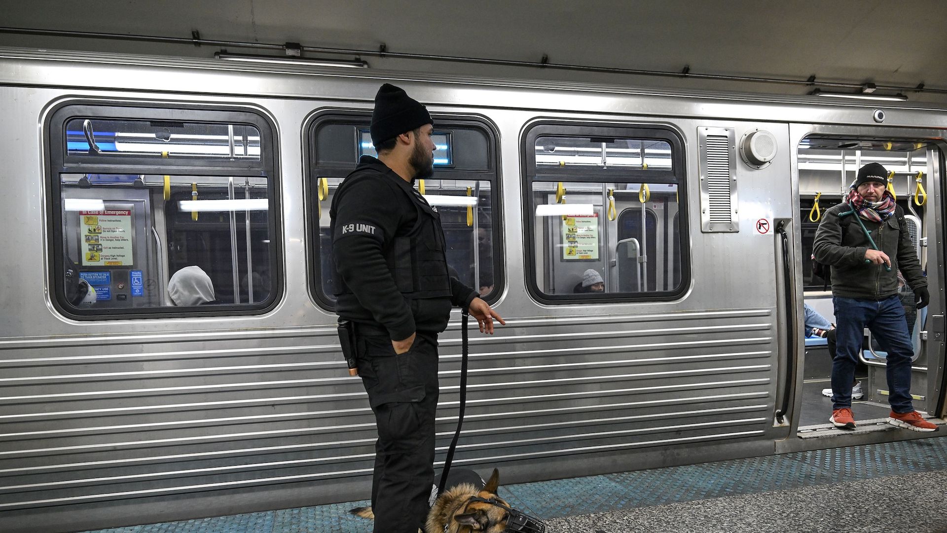 A security guard with a K-9 stands outside a subway train as a man gets off the train.